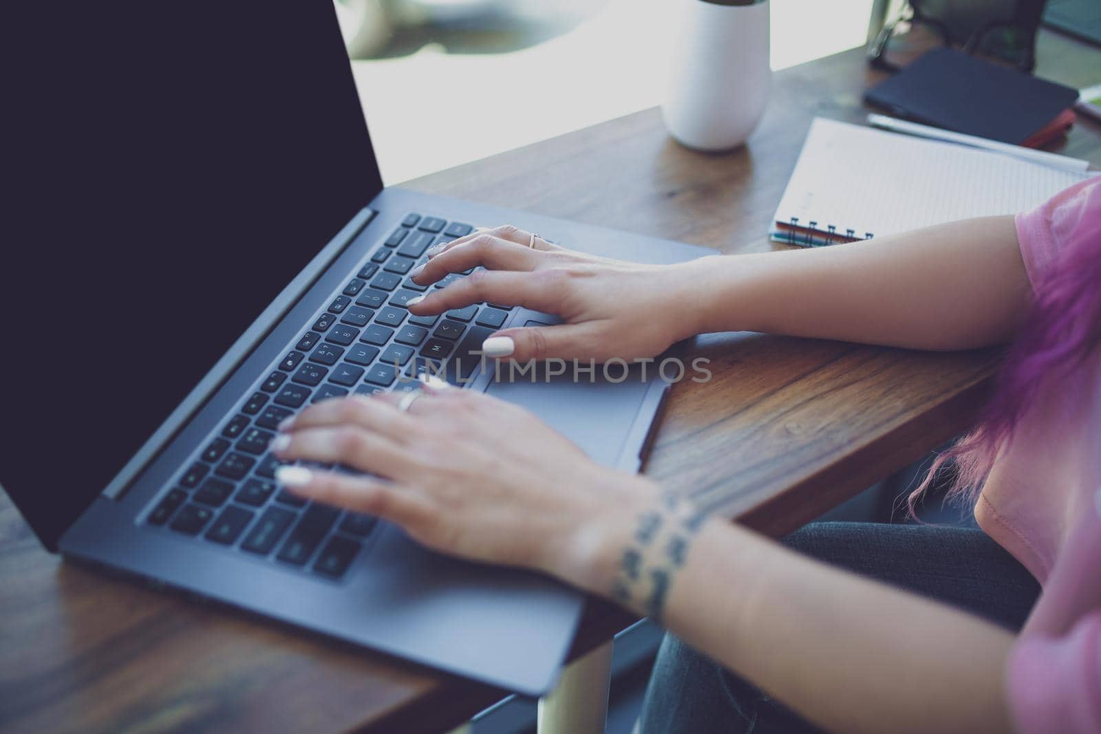 Back view of a young pink hair woman keyboarding on laptop computer with blank copy space screen while sitting in cafe, intelligent female student working on net-book after her lectures in University