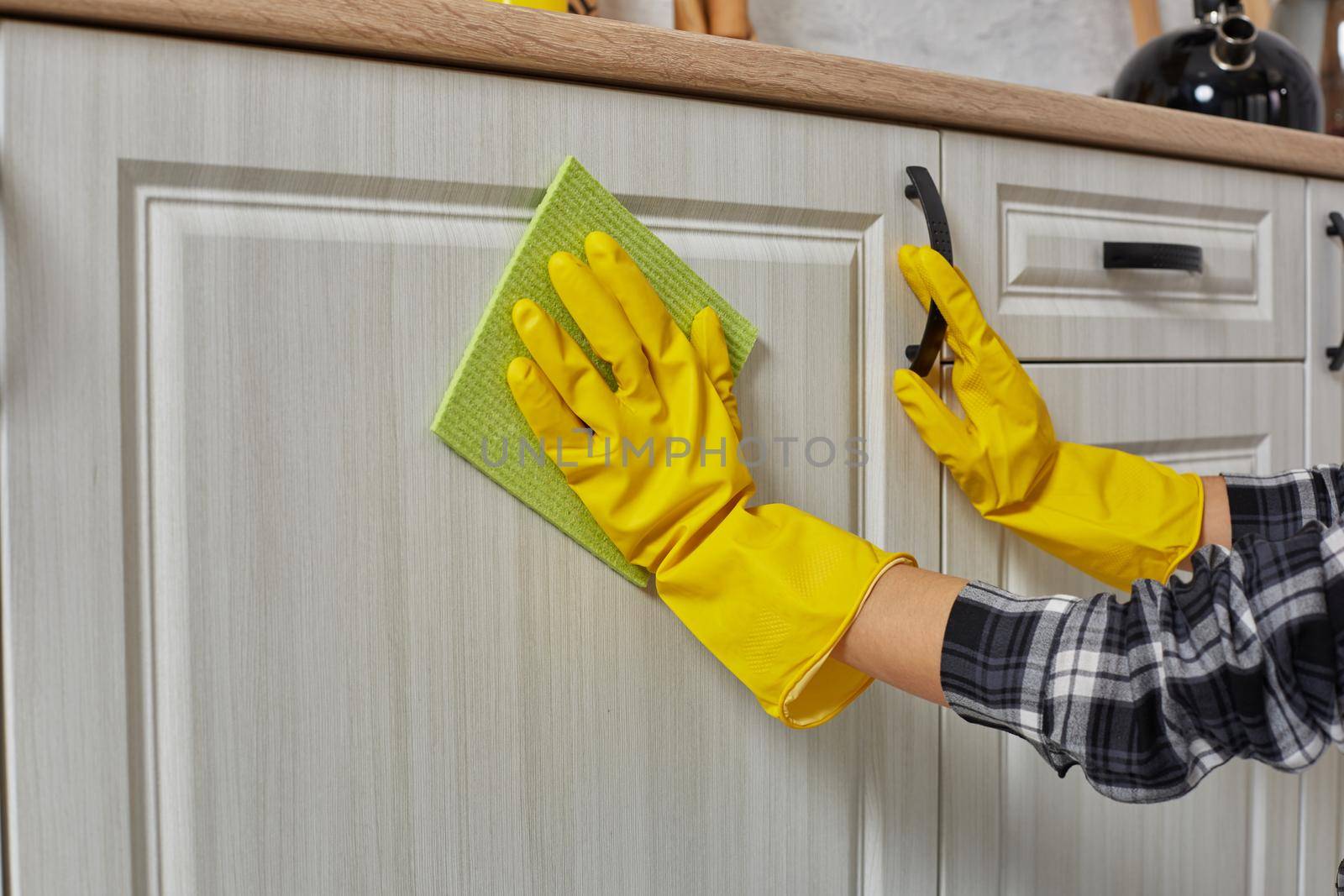 Hands in gloves with green rag is cleaning kitchen cabinets - housework and housekeeping concept. Close-up