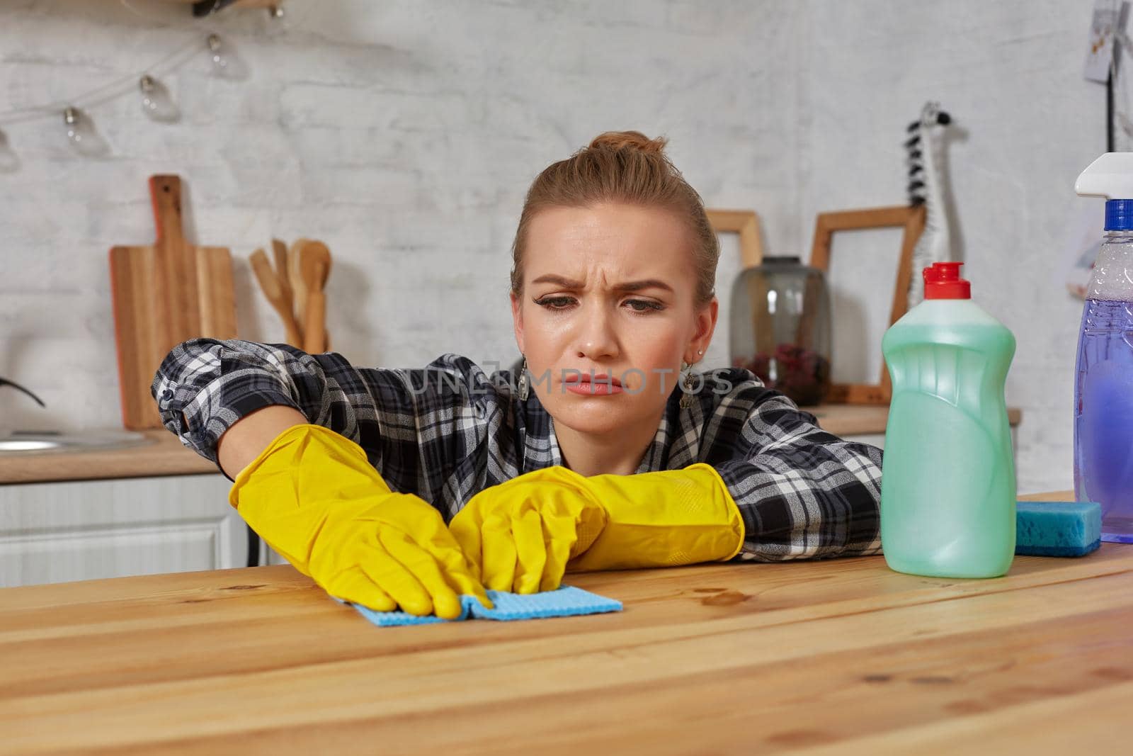 Young woman in protective gloves wipes a table in the kitchen with a rag. Fatigue. Household, cleaning and people concept