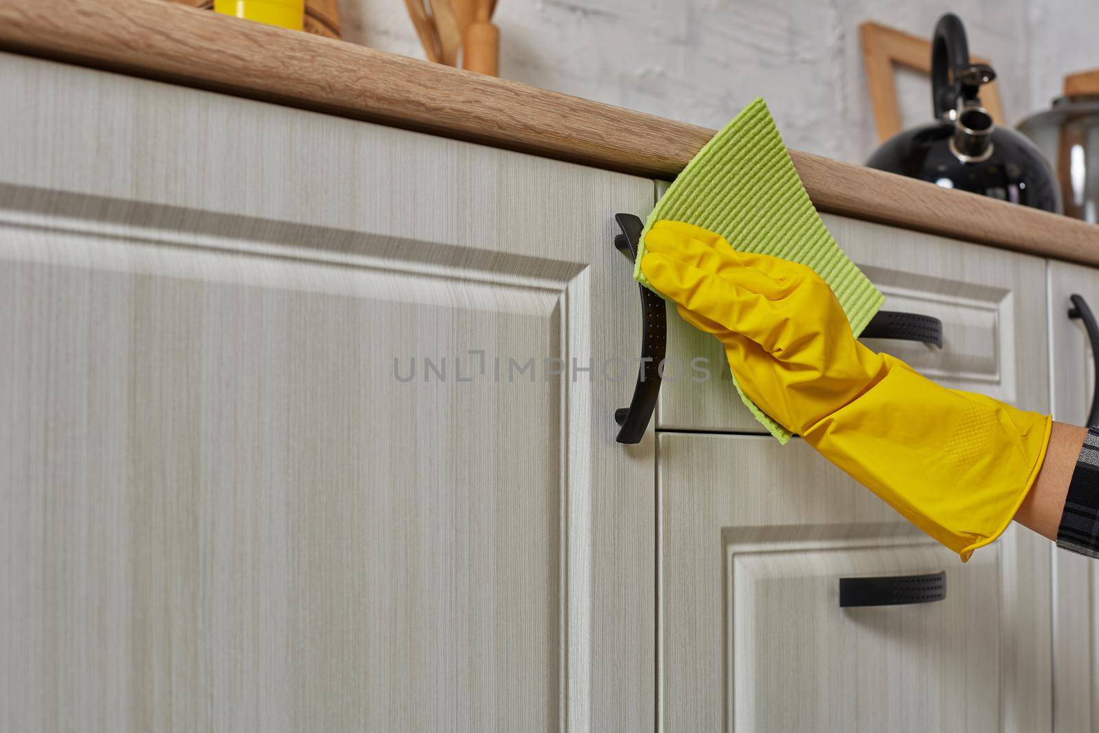 Hands in gloves with green rag is cleaning kitchen cabinets - housework and housekeeping concept. Close-up