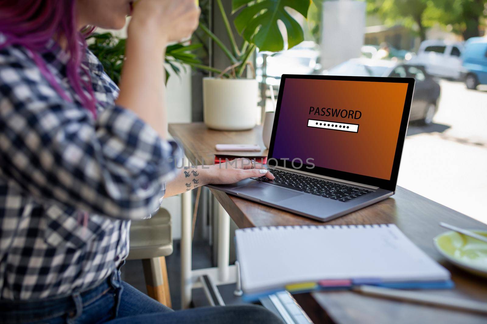 Side view of a young pink hair woman sitting in cafe, hand typing laptop computer with password login on screen. Cyber security concept