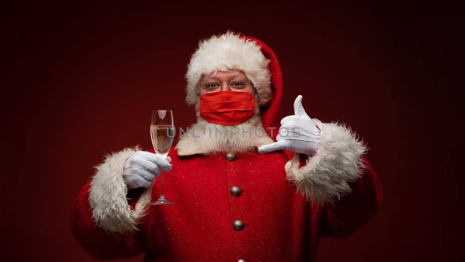 Santa Claus in facial protective mask holding glass of champagne and showing call finger sign