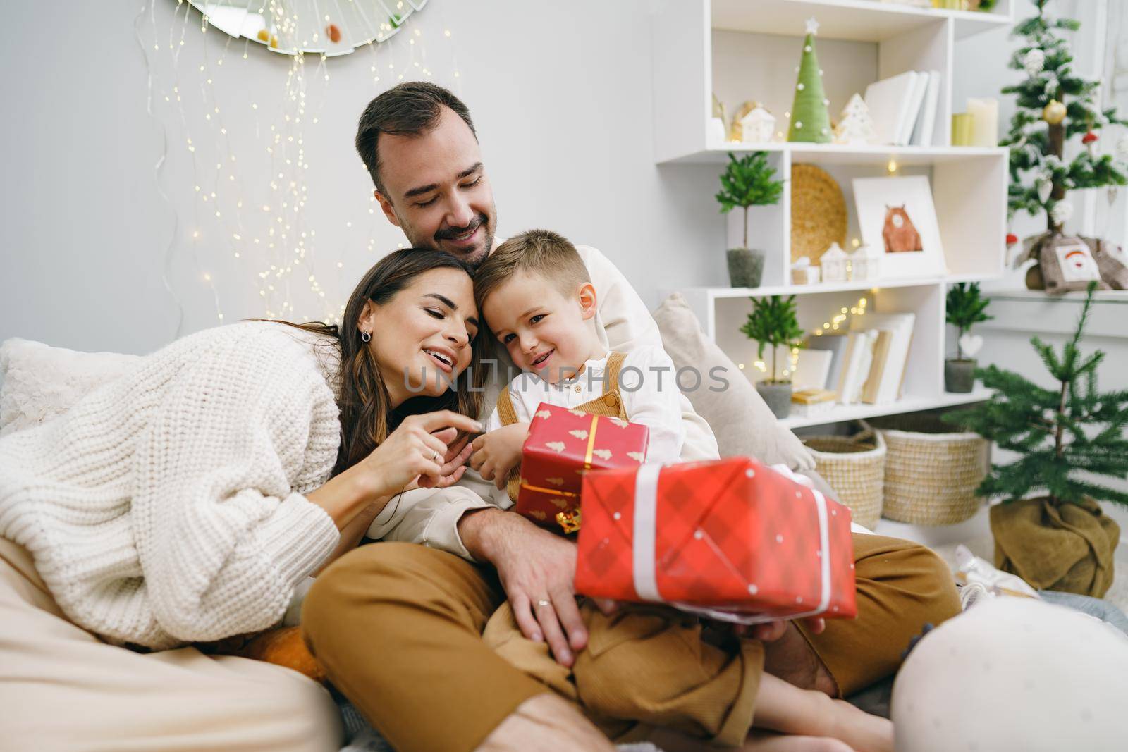 Smiling parents giving Christmas present to son at home by Fabrikasimf