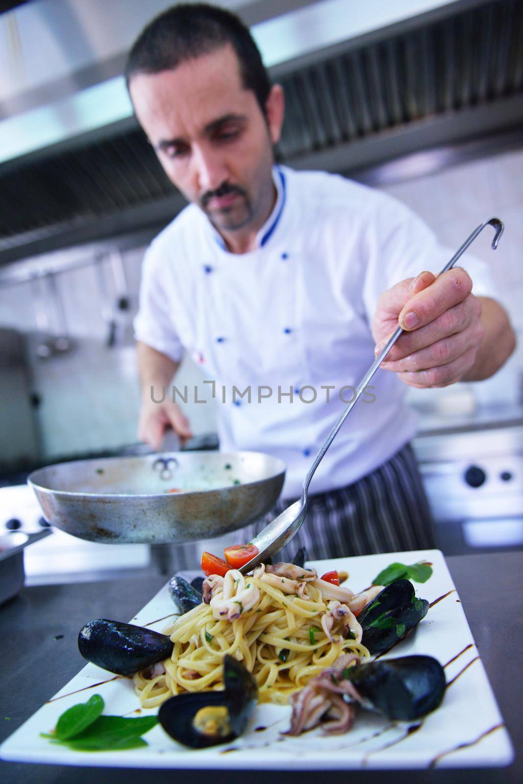 Handsome chef dressed in white uniform decorating pasta salad and seafood fish in modern kitchen