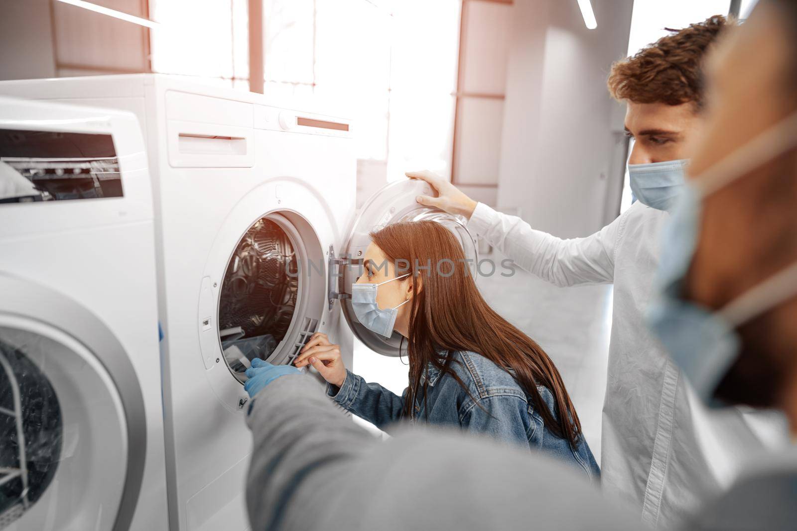 Salesman in hypermarket wearing medical mask demonstrates his clients a new washing machine by Fabrikasimf