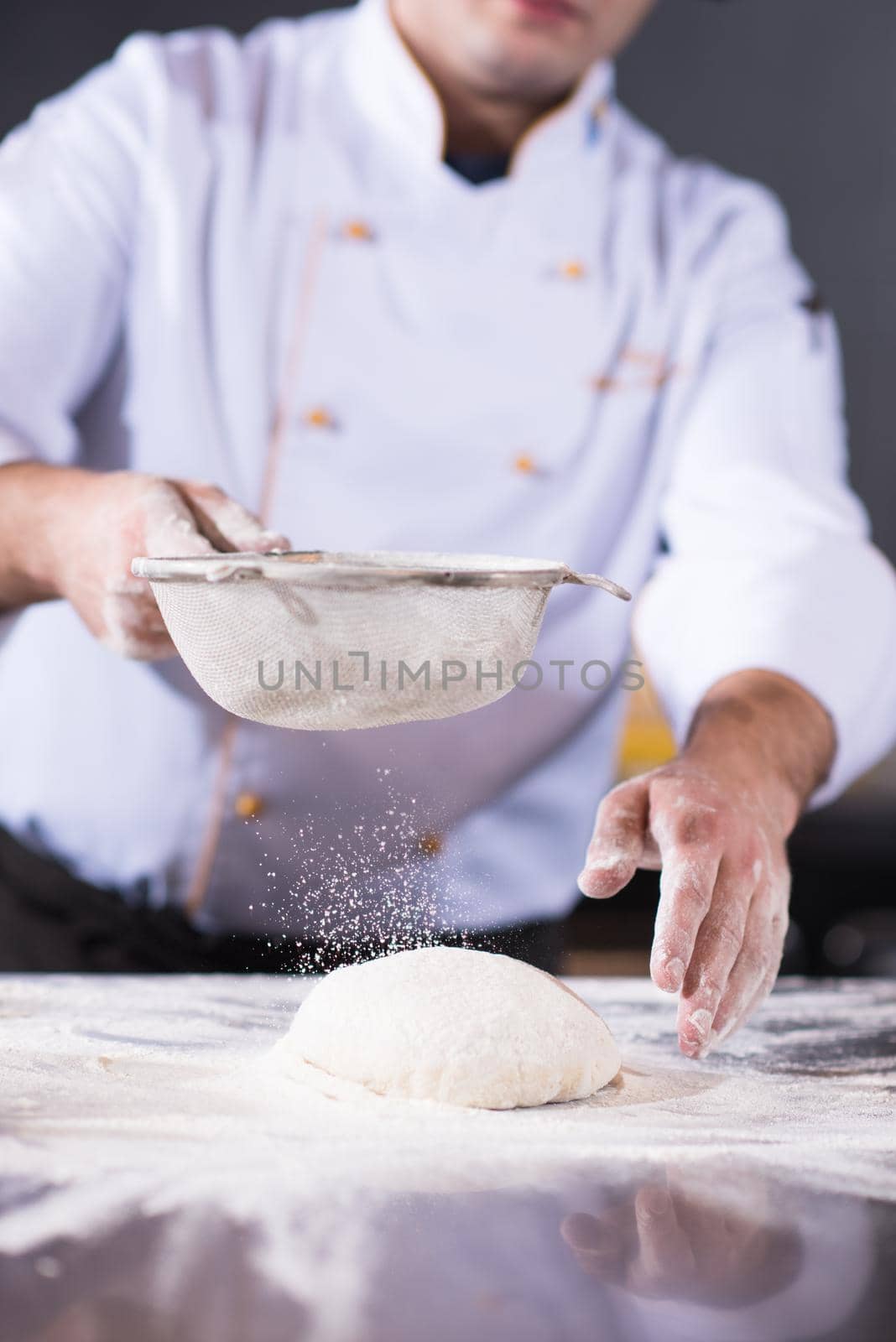 chef sprinkling flour over fresh pizza dough on kitchen table