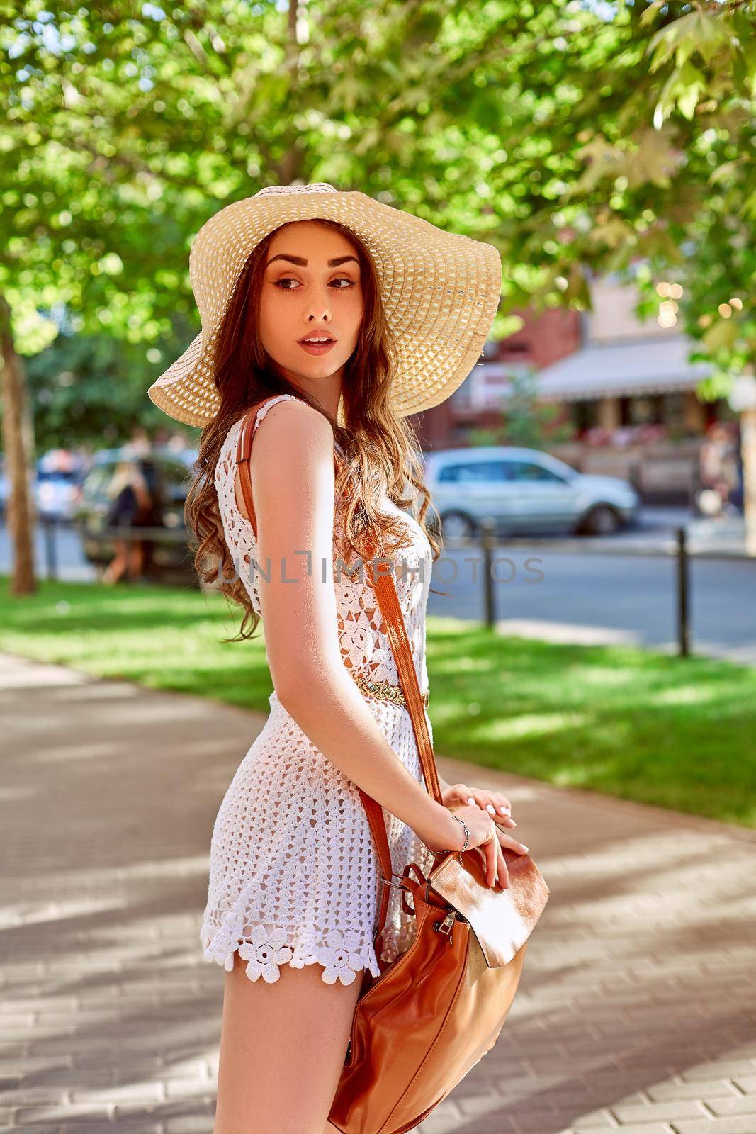 Sunny lifestyle fashion portrait of young stylish hipster woman walking on the street, wearing trendy outfit, straw hat, travel with backpack. Street style