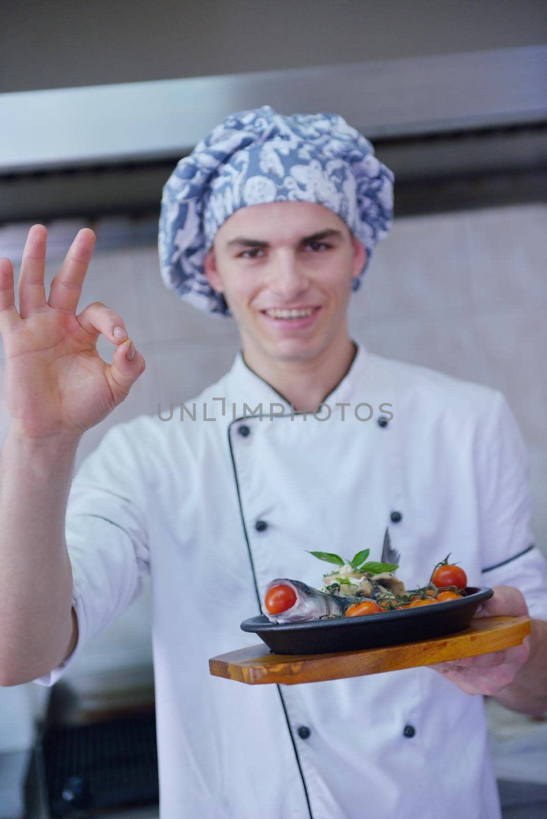 Handsome chef dressed in white uniform decorating pasta salad and seafood fish in modern kitchen