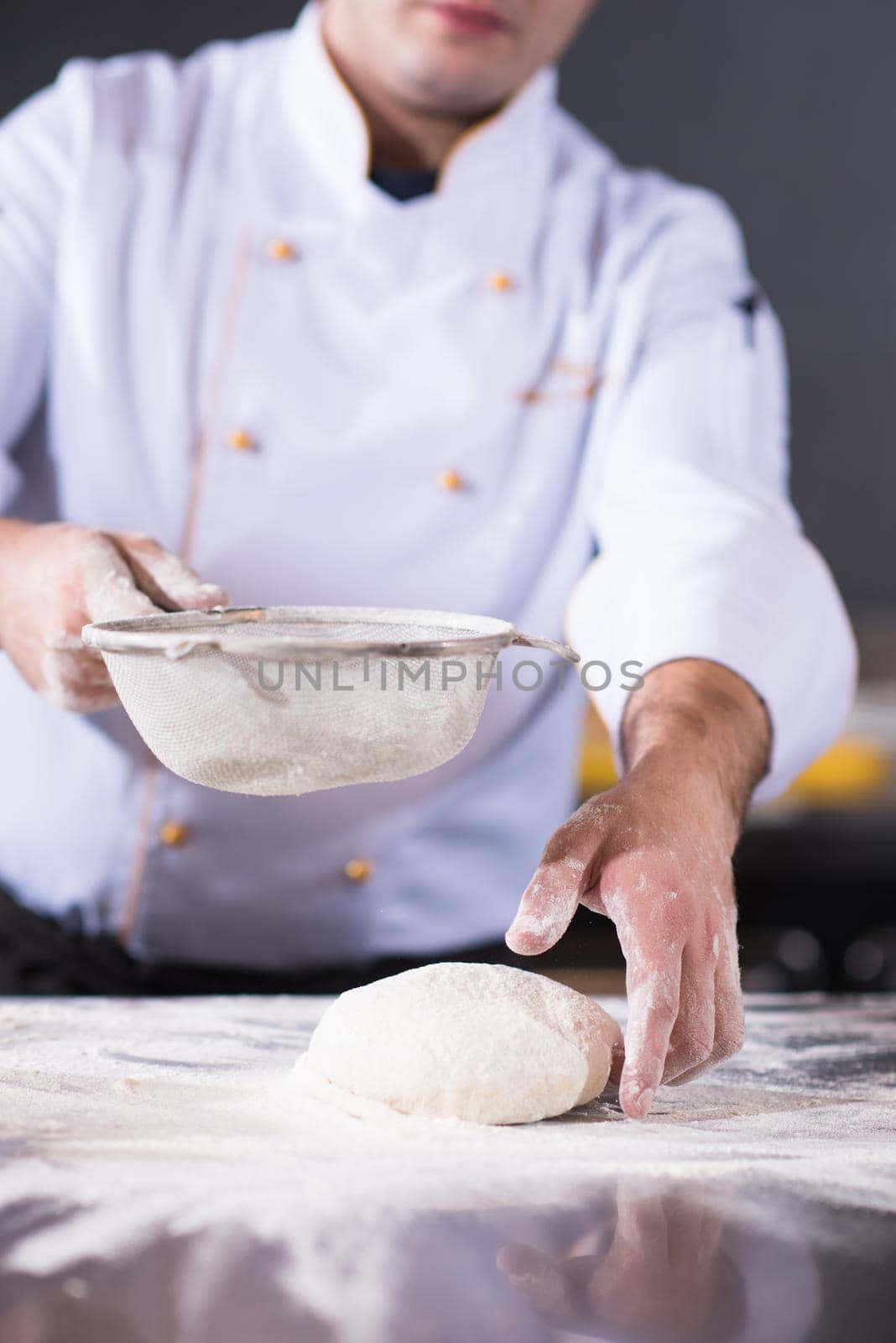 chef sprinkling flour over fresh pizza dough on kitchen table