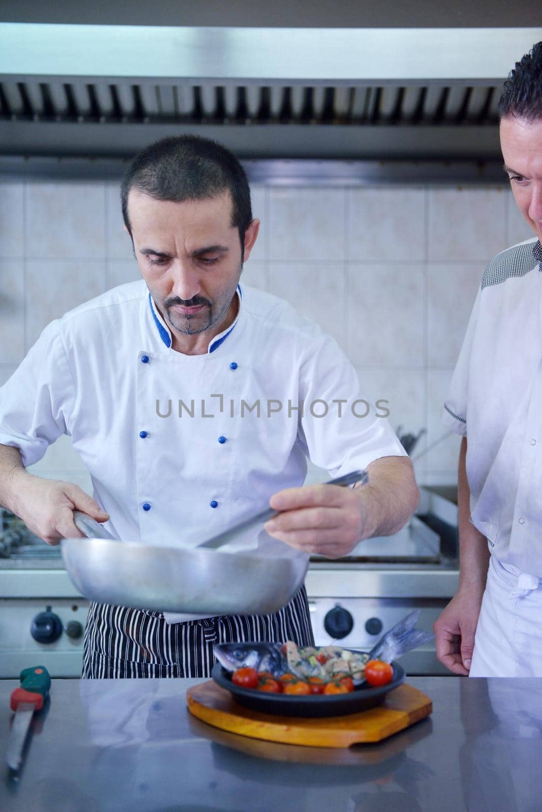 Handsome chef dressed in white uniform decorating pasta salad and seafood fish in modern kitchen