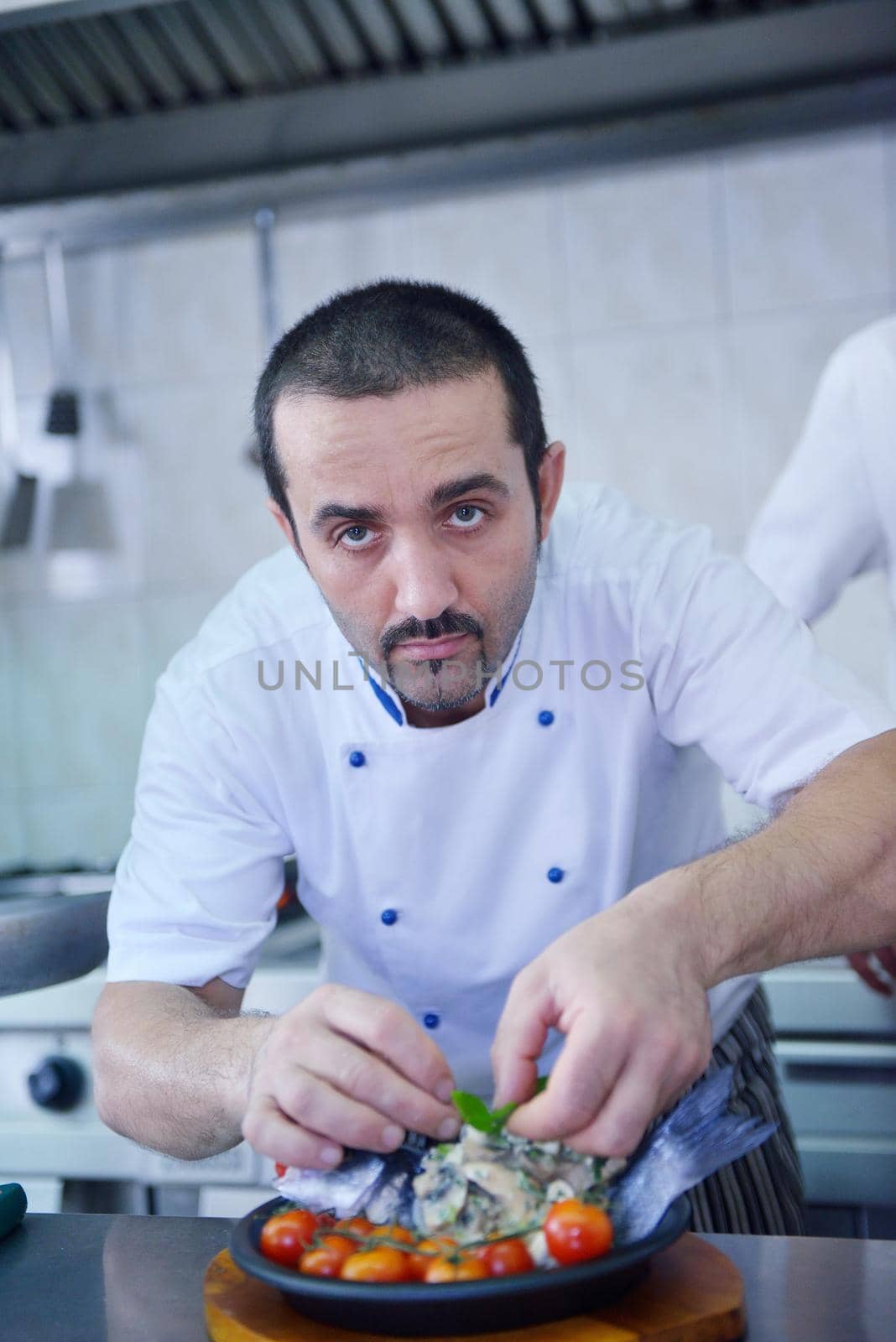 Handsome chef dressed in white uniform decorating pasta salad and seafood fish in modern kitchen