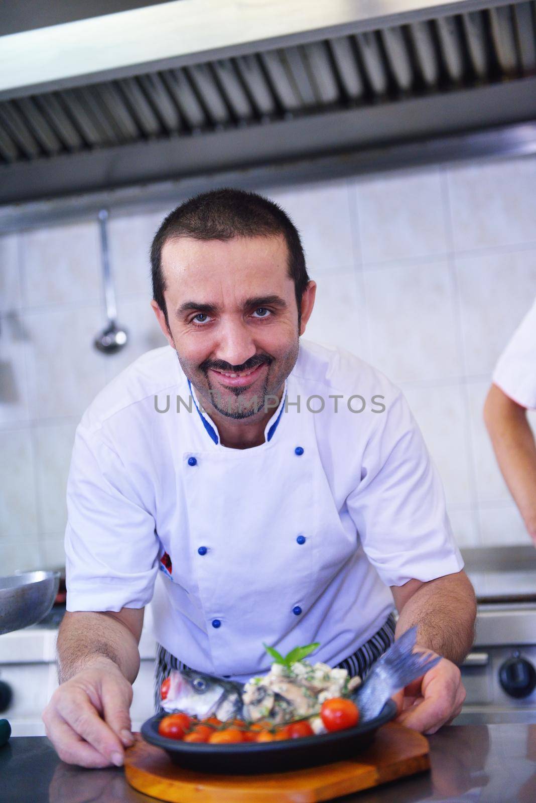 Handsome chef dressed in white uniform decorating pasta salad and seafood fish in modern kitchen