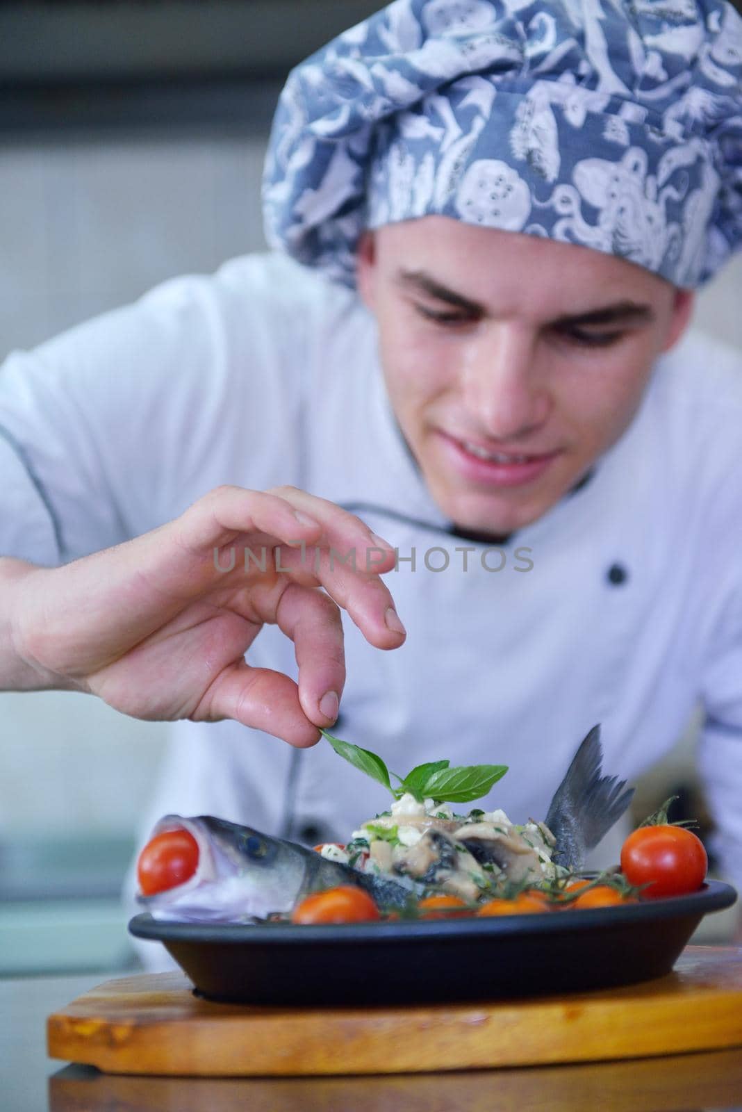 Handsome chef dressed in white uniform decorating pasta salad and seafood fish in modern kitchen