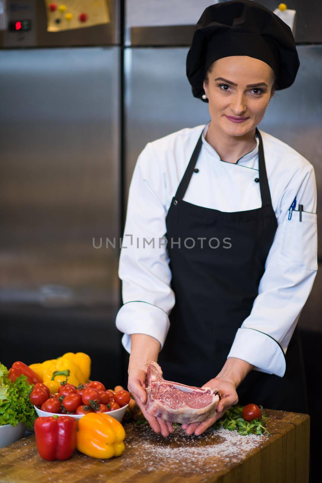 Master Chef holding juicy slice of raw steak with vegetables around on a wooden table