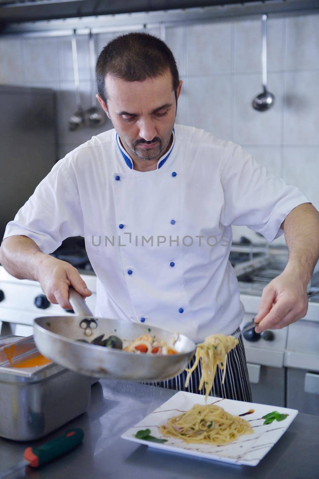 Handsome chef dressed in white uniform decorating pasta salad and seafood fish in modern kitchen