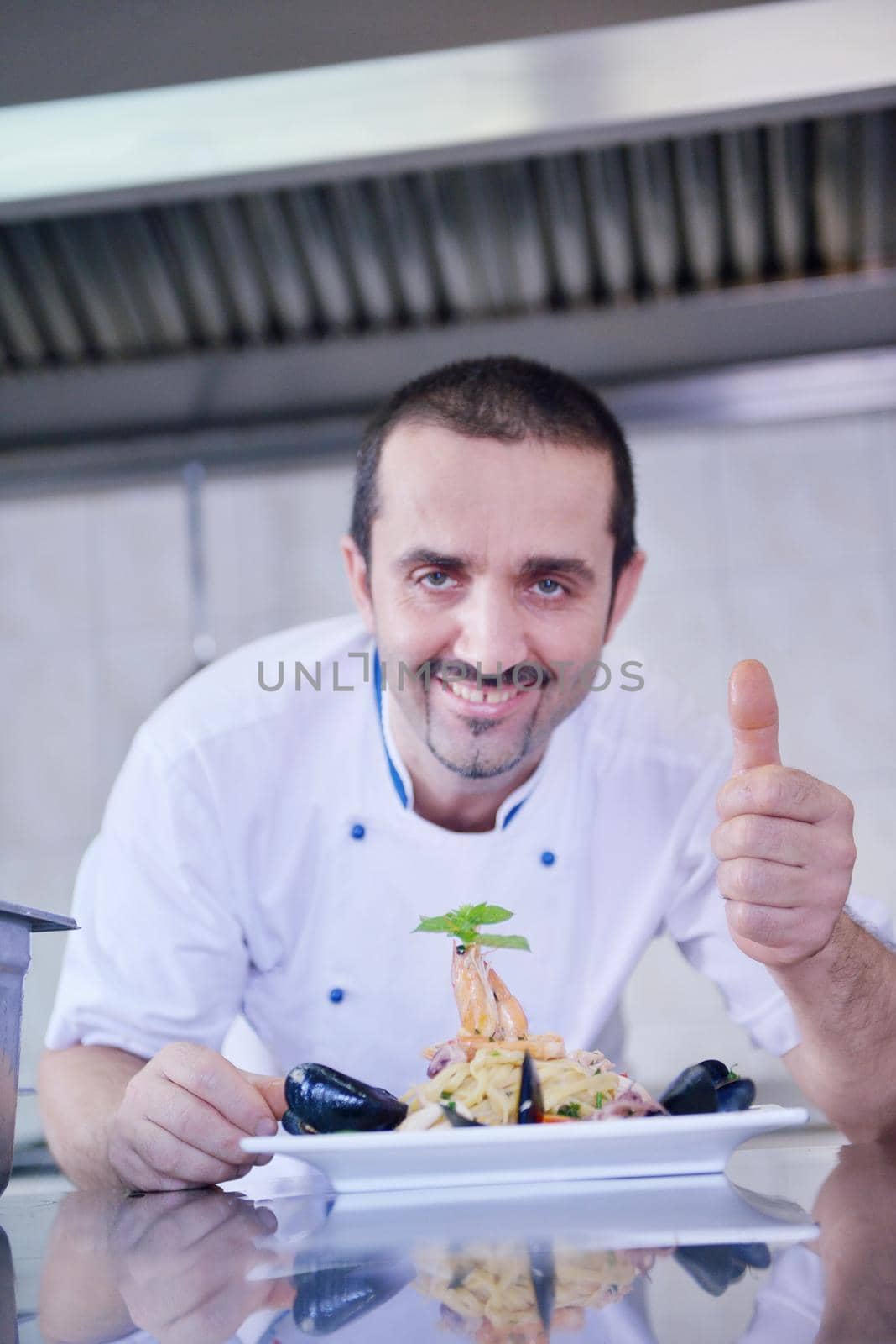 Handsome chef dressed in white uniform decorating pasta salad and seafood fish in modern kitchen