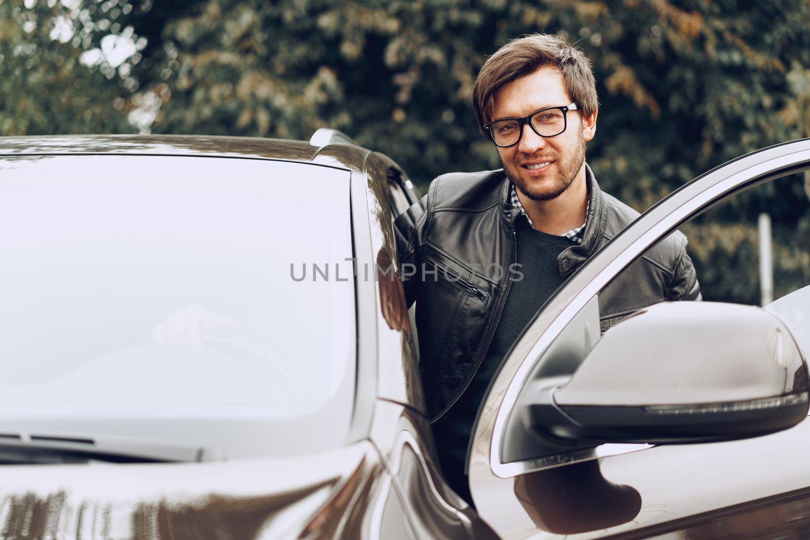 Stylish man in glasses sits in a car, close up portrait