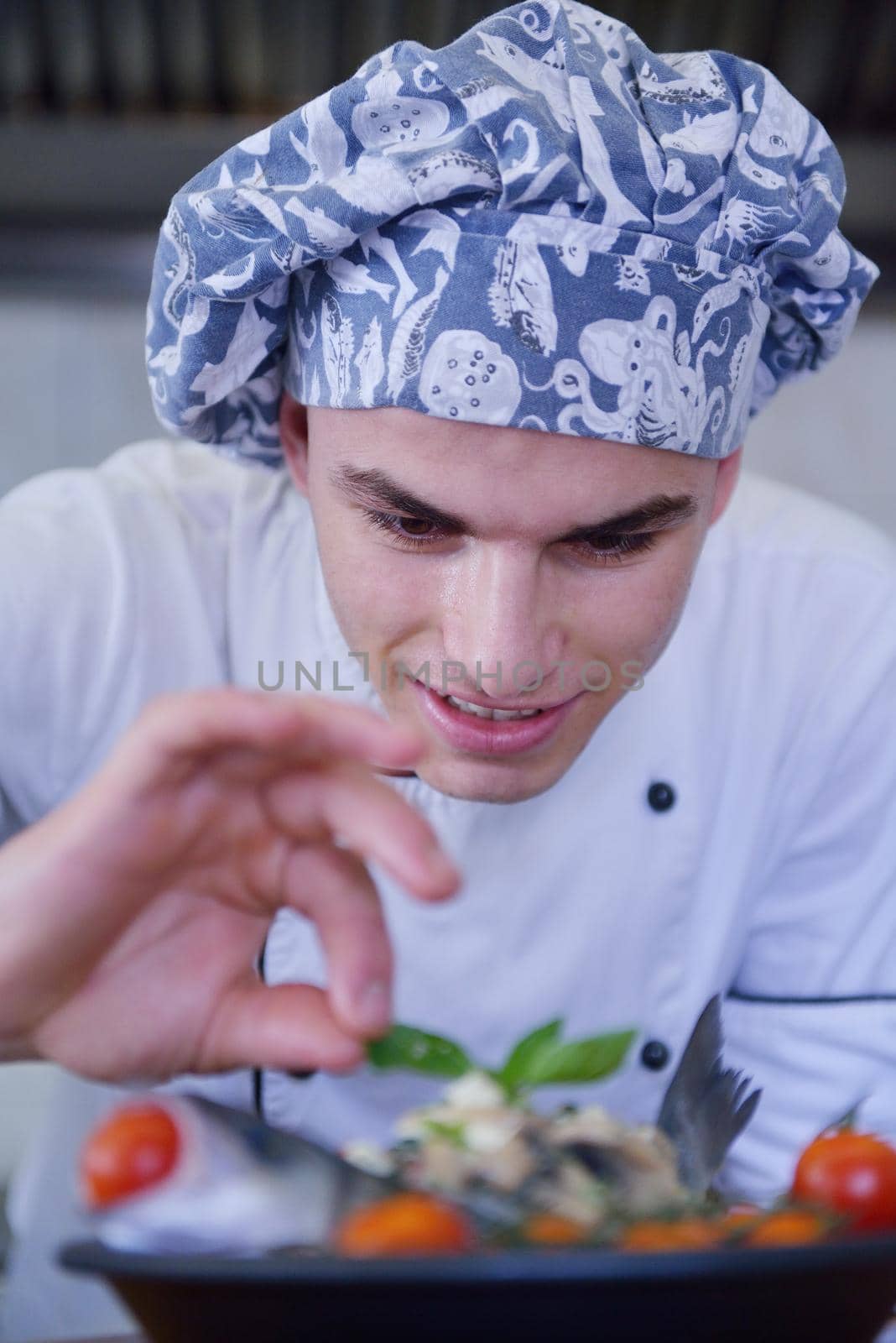 Handsome chef dressed in white uniform decorating pasta salad and seafood fish in modern kitchen