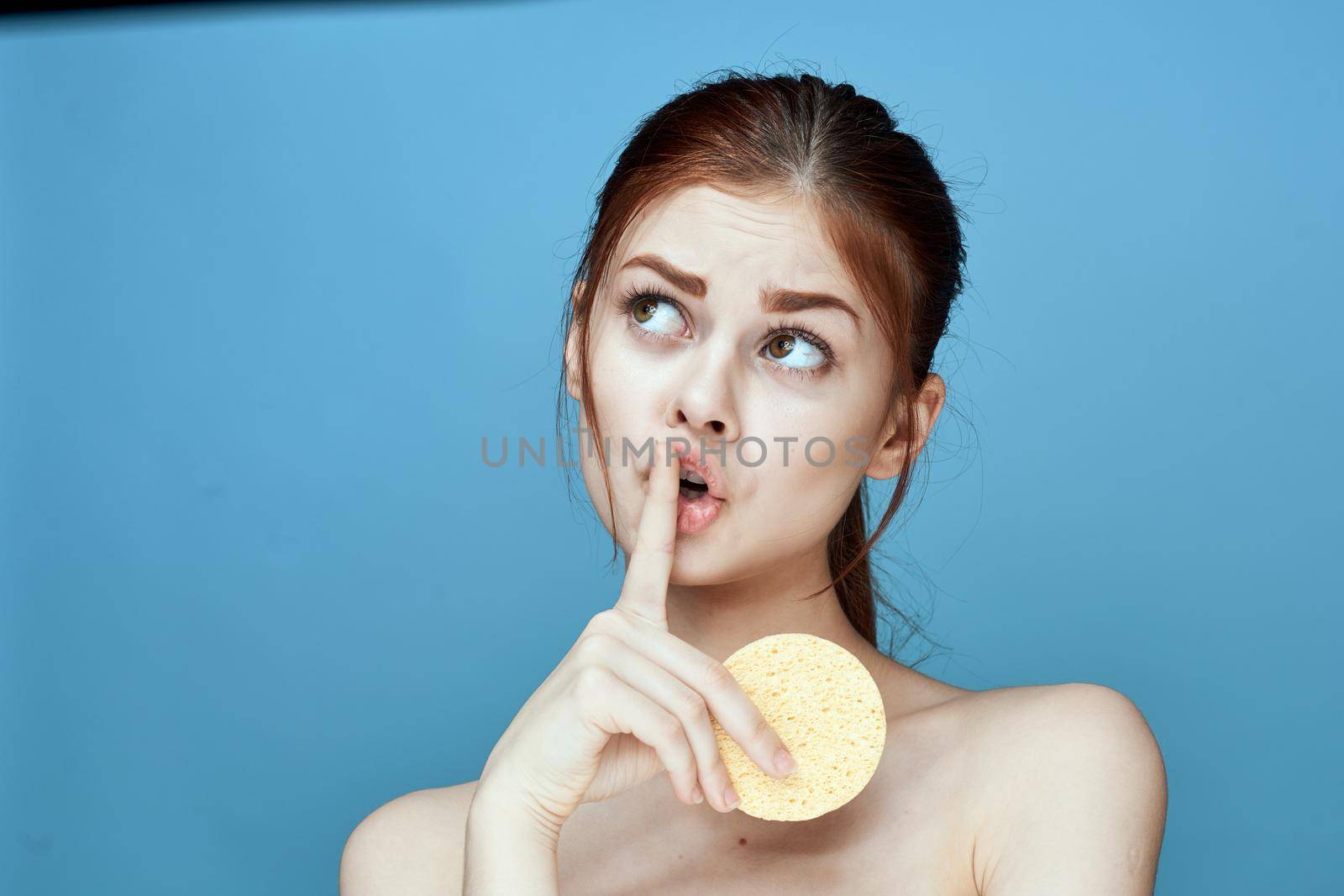 woman with sponges in hands bare shoulders clear skin blue background. High quality photo