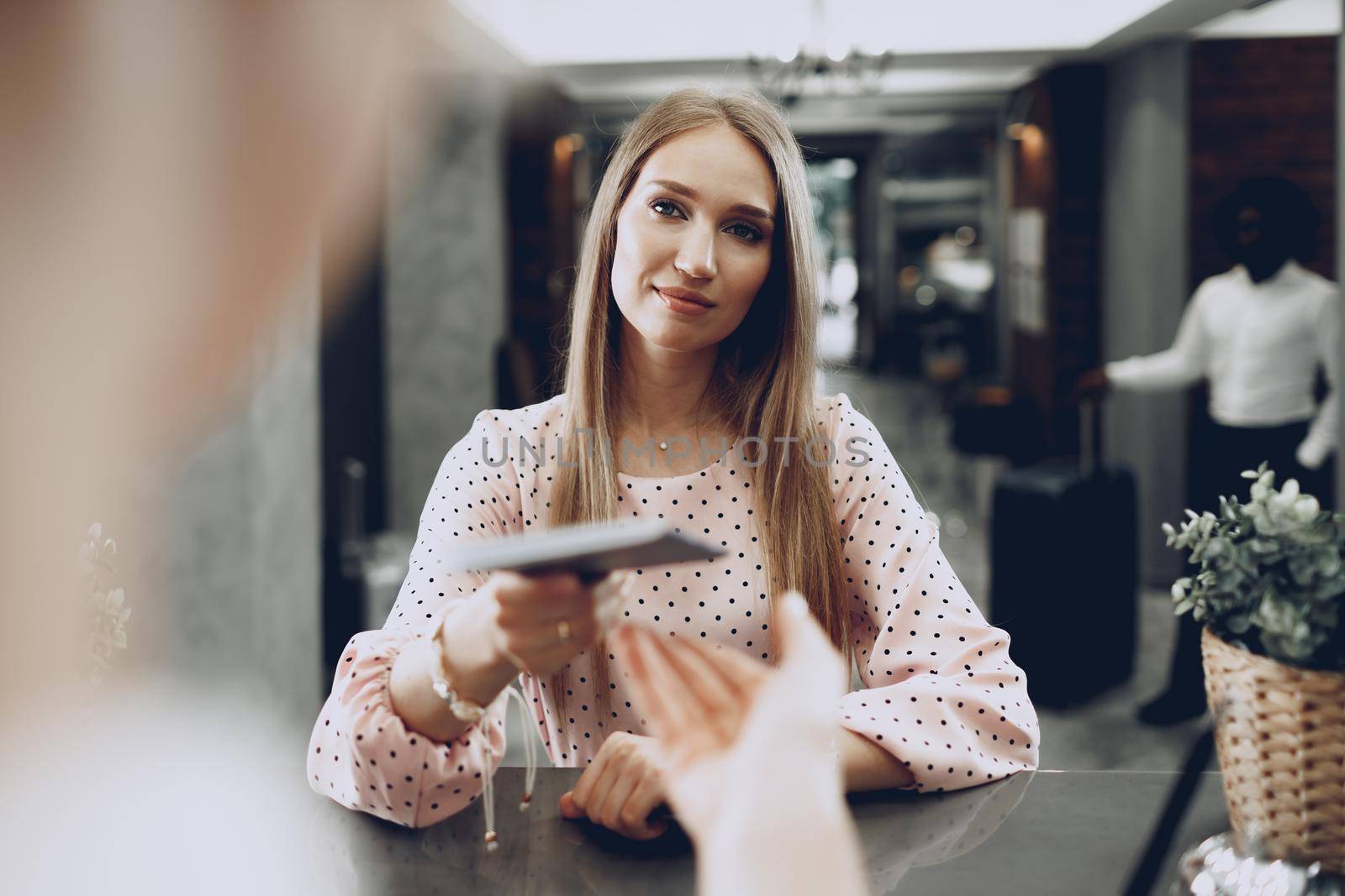 Blonde woman hotel guest checking-in at front desk in hotel close up