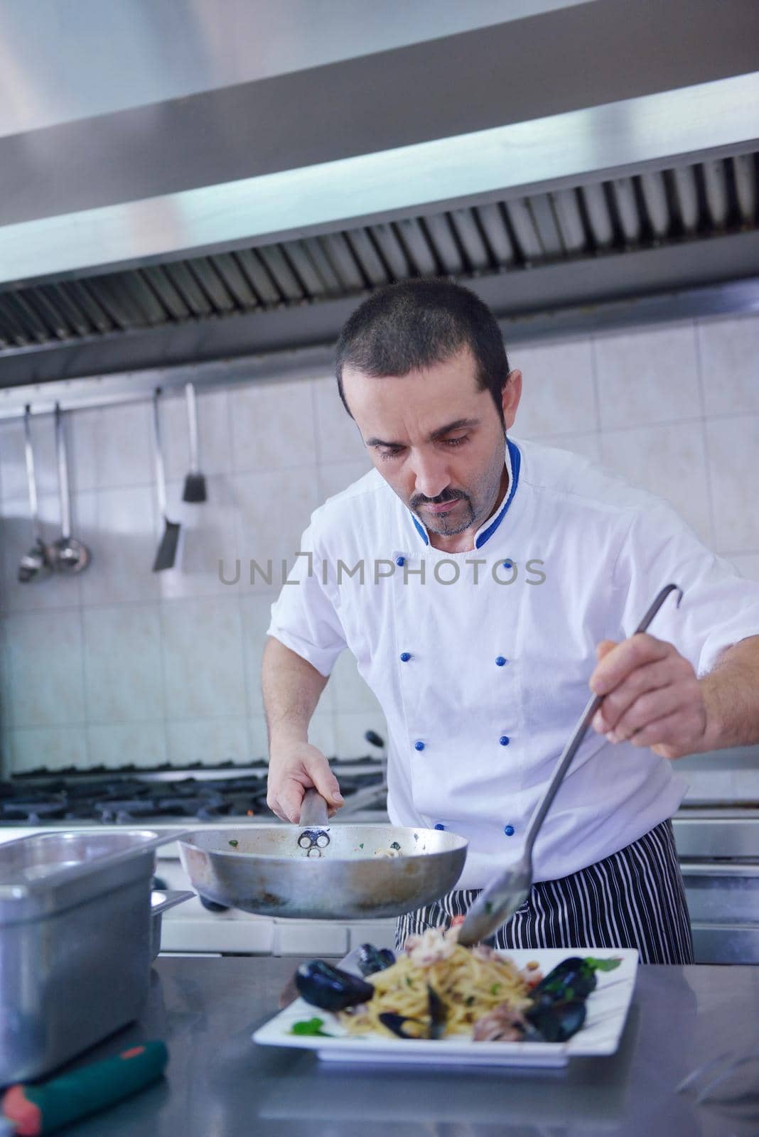 Handsome chef dressed in white uniform decorating pasta salad and seafood fish in modern kitchen