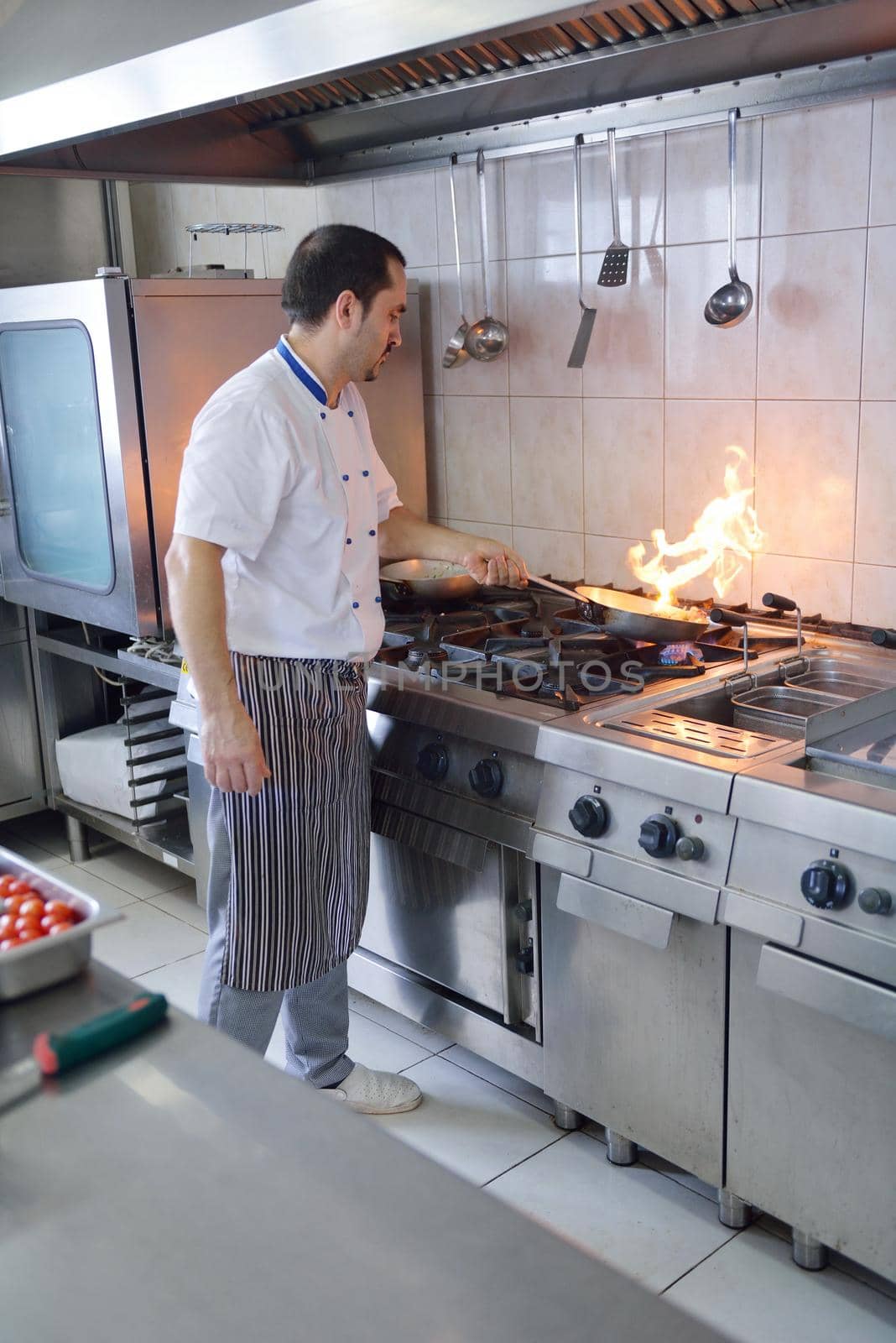 Handsome chef dressed in white uniform decorating pasta salad and seafood fish in modern kitchen