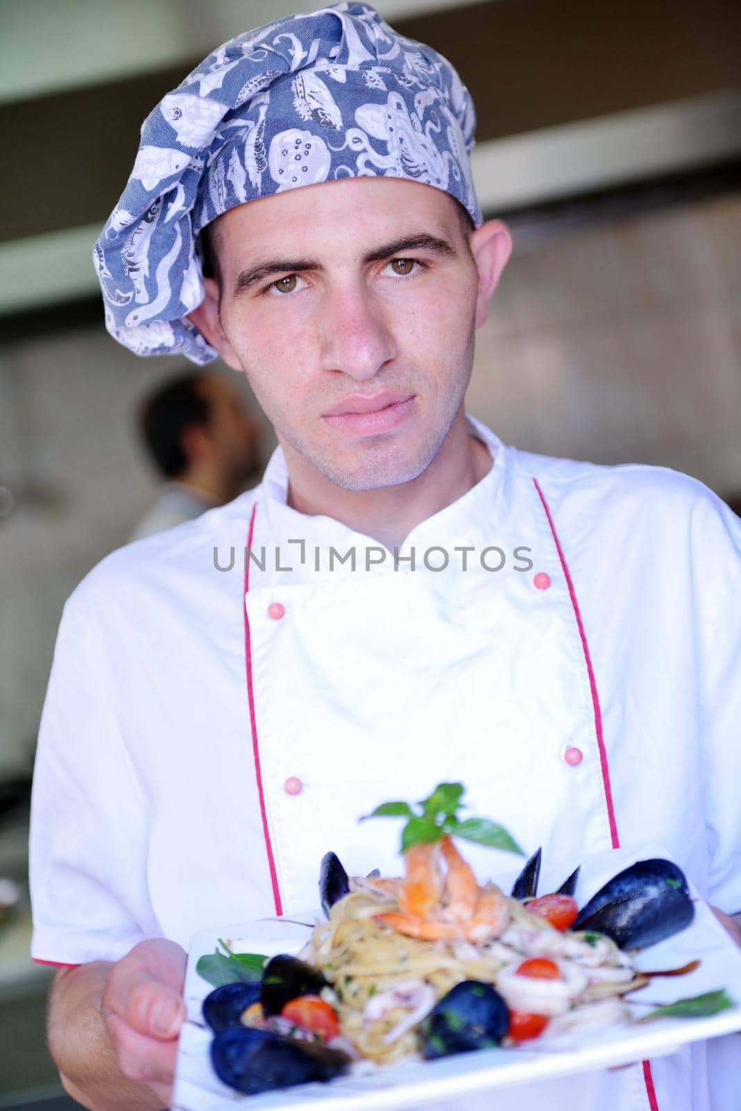 Handsome chef dressed in white uniform decorating pasta salad and seafood fish in modern kitchen