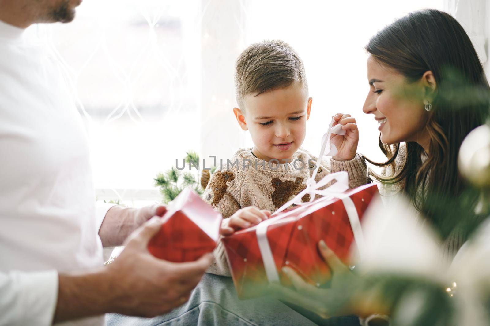 Smiling parents giving Christmas present to son at home by Fabrikasimf