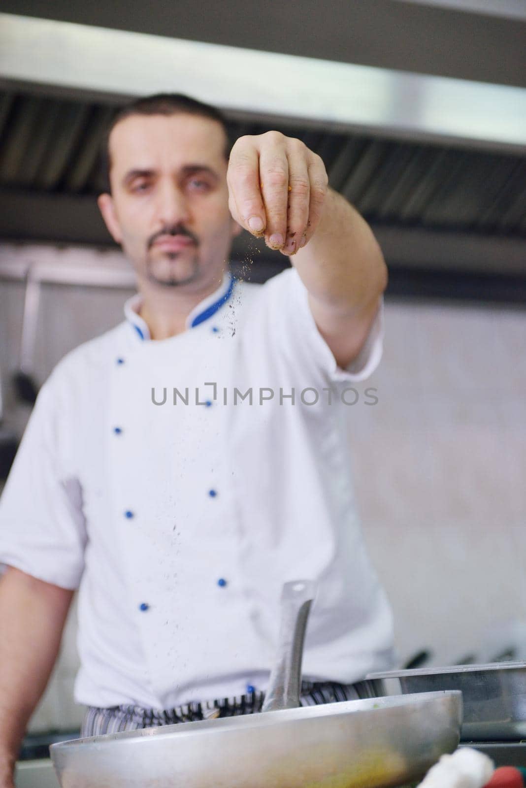 Handsome chef dressed in white uniform decorating pasta salad and seafood fish in modern kitchen