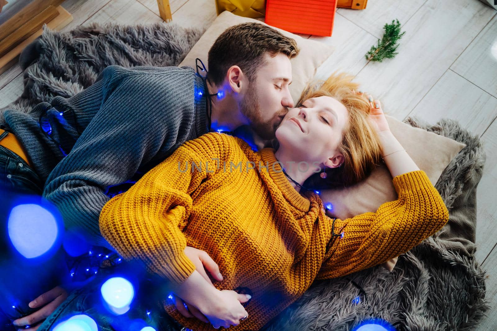A beautiful and happy couple lies on a gray fluffy bedspread in a Christmas blue garland.