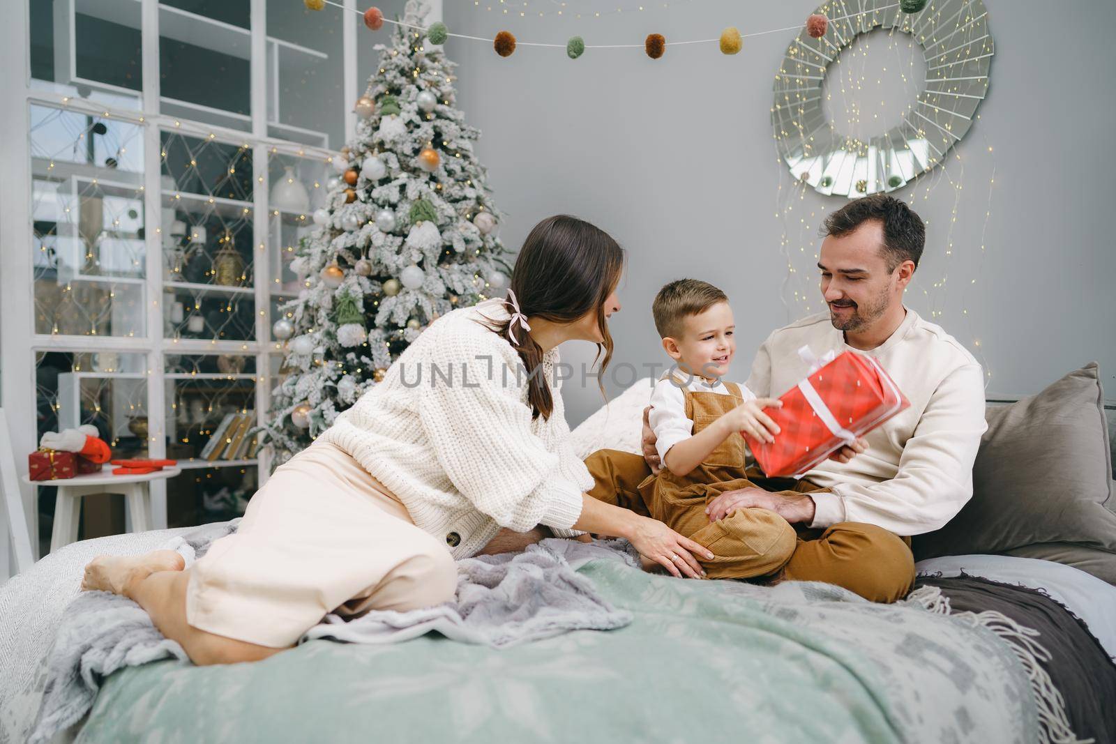 Smiling parents giving Christmas present to son at home by Fabrikasimf