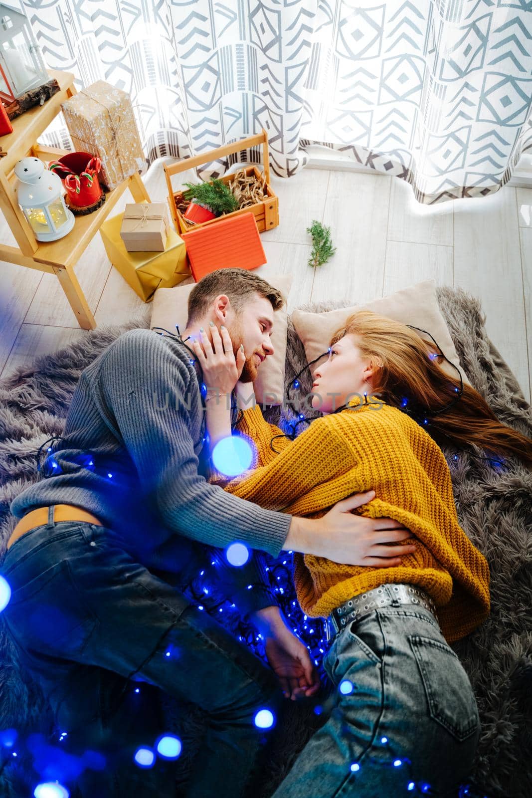 Beautiful and happy couple lies on a gray fluffy bedspread in a Christmas blue garland.