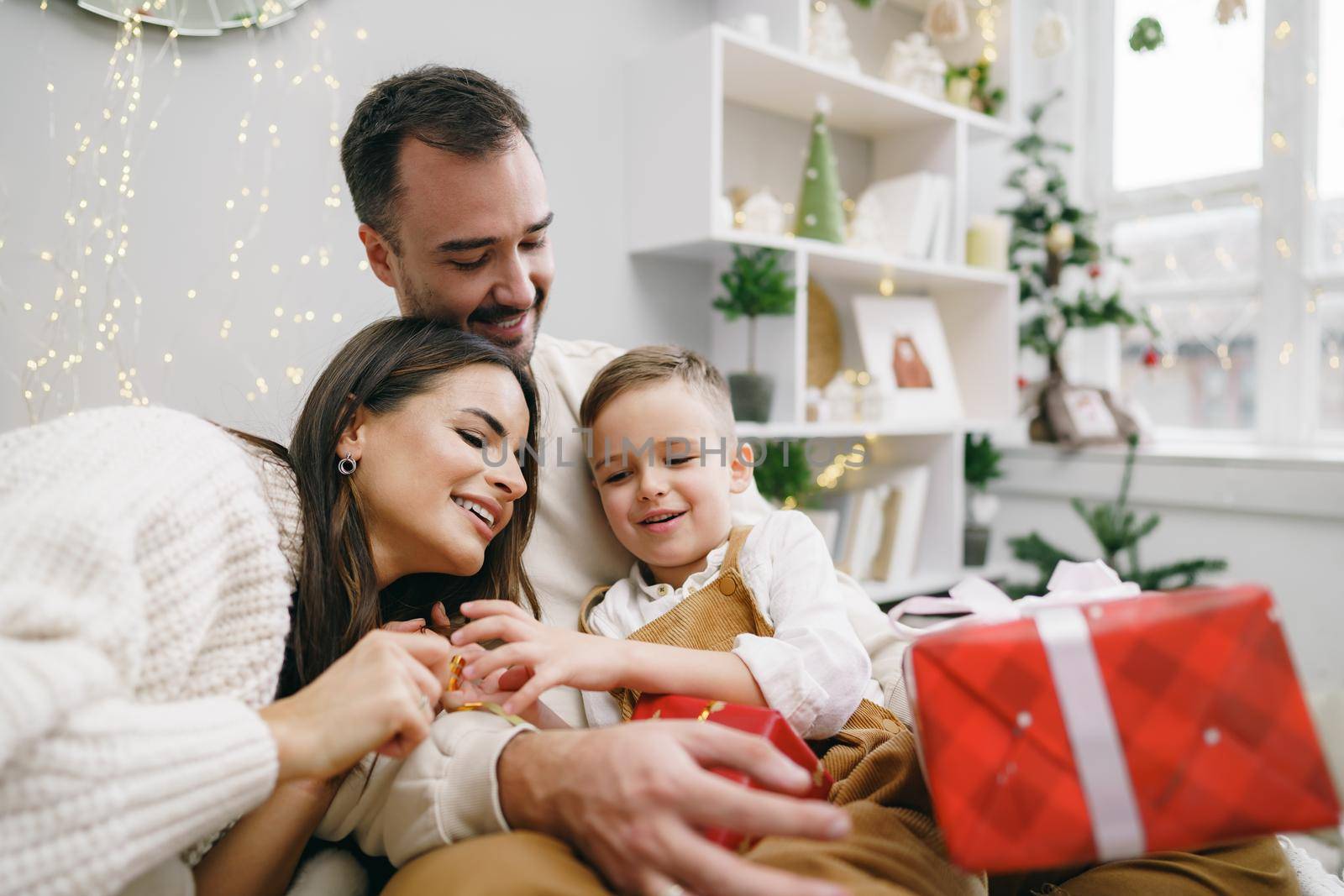 Smiling parents giving Christmas present to son at home by Fabrikasimf