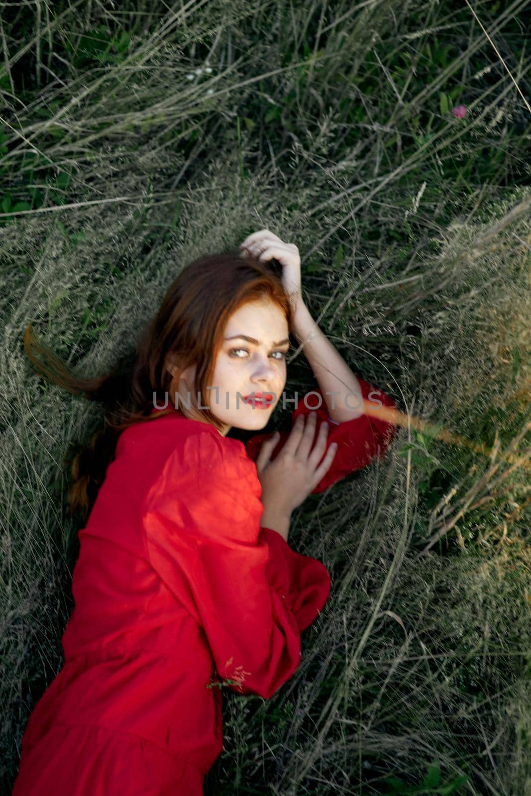 pretty woman in red dress lies on the grass posing top view. High quality photo