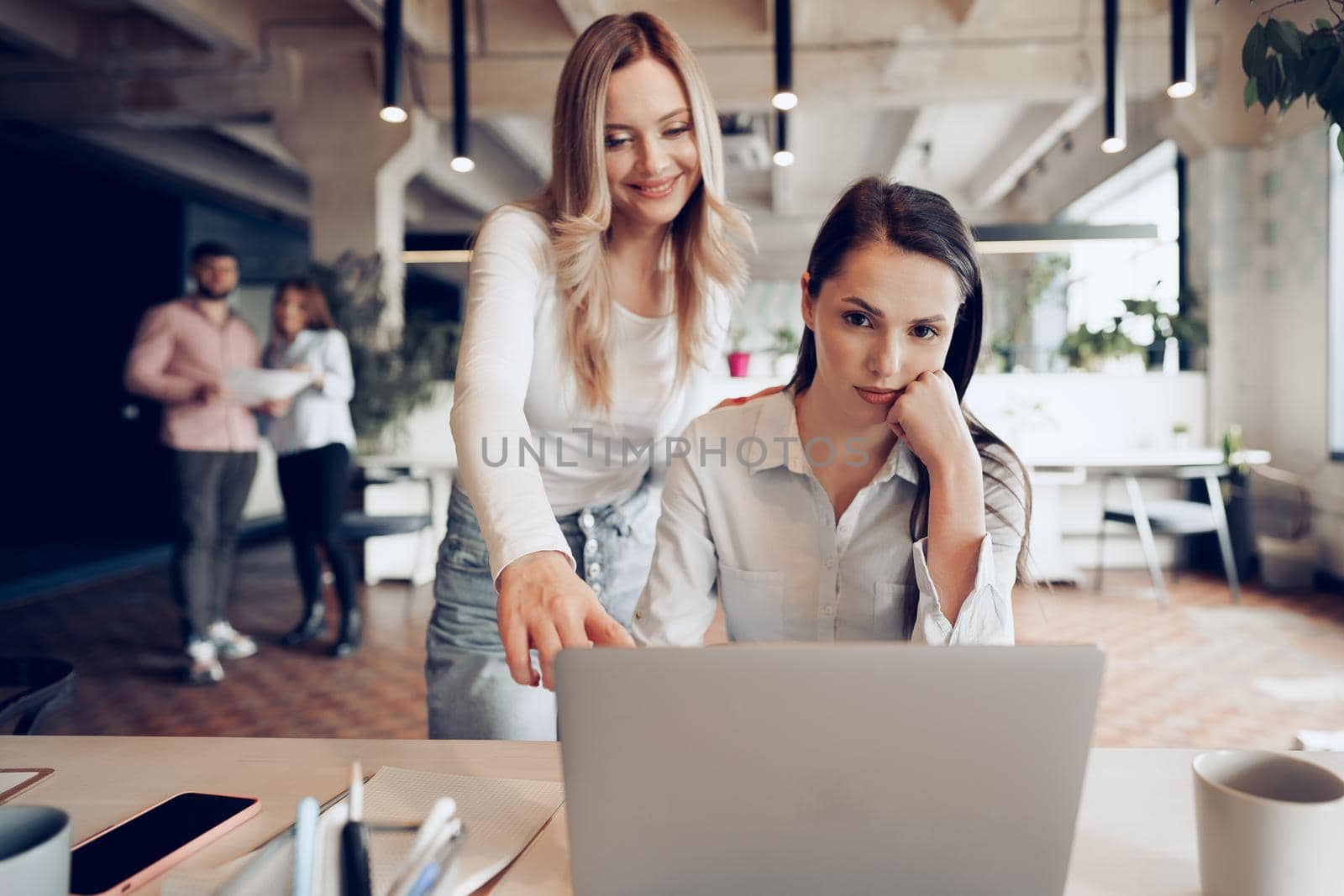 Two young female colleagues discussing business project together in modern office
