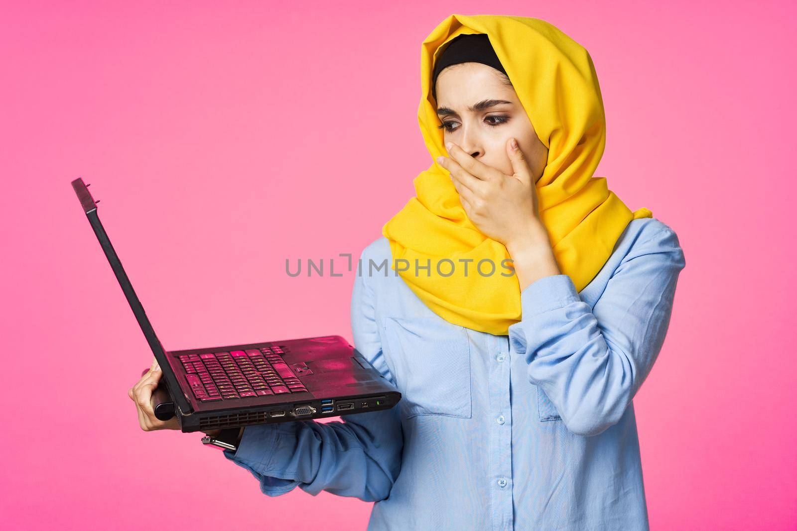 muslim woman in yellow hijab with laptop technology student pink background. High quality photo
