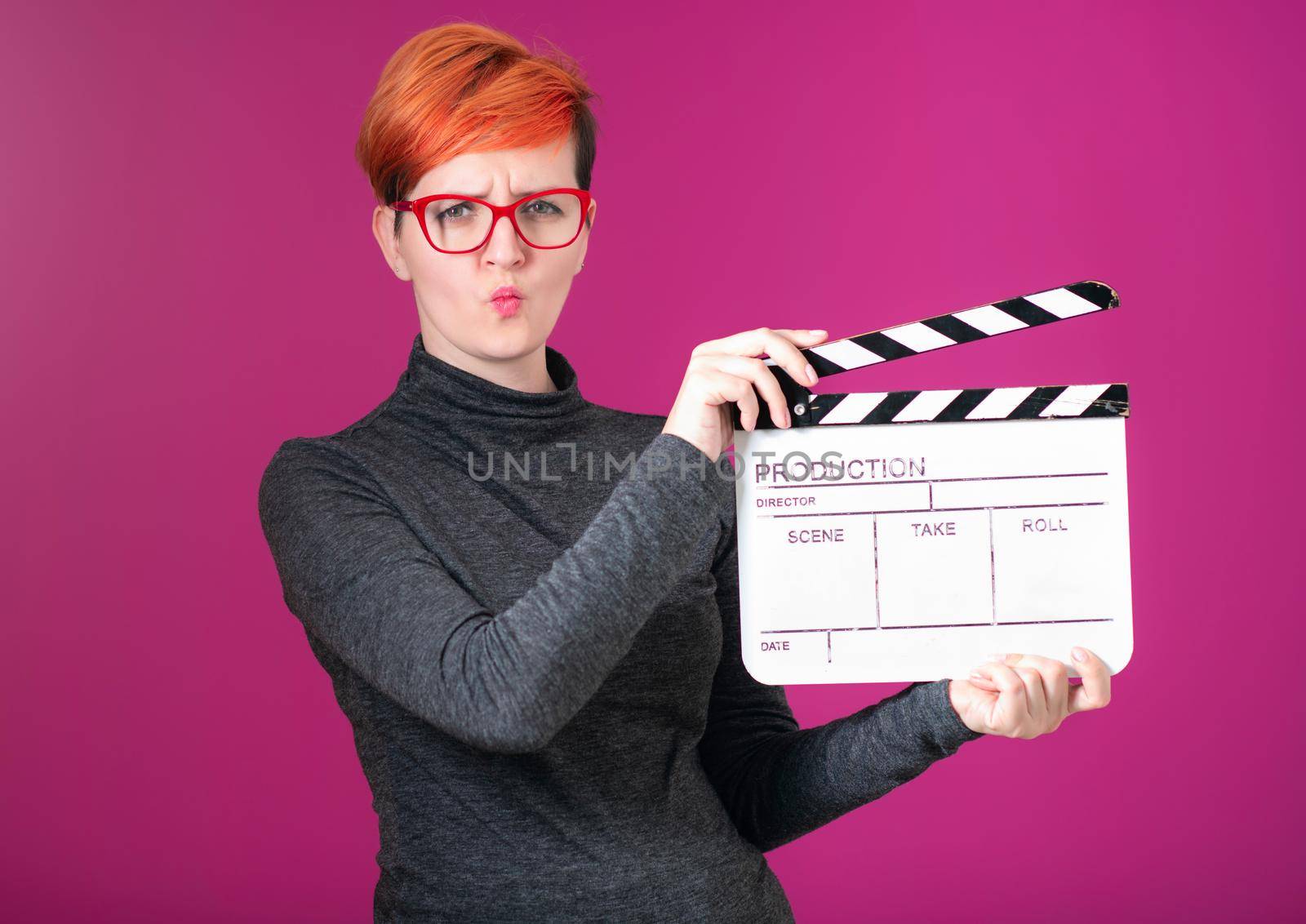 redhead woman holding movie  clapper on pink background by dotshock