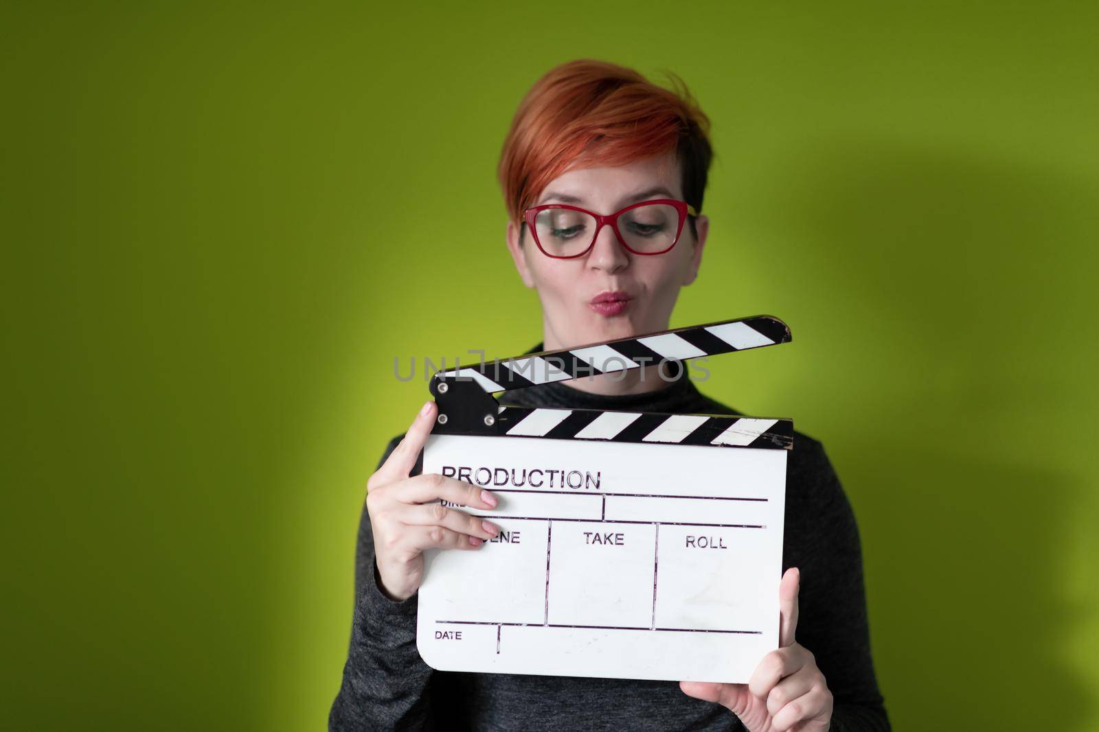 redhead woman holding movie  clapper on green background by dotshock