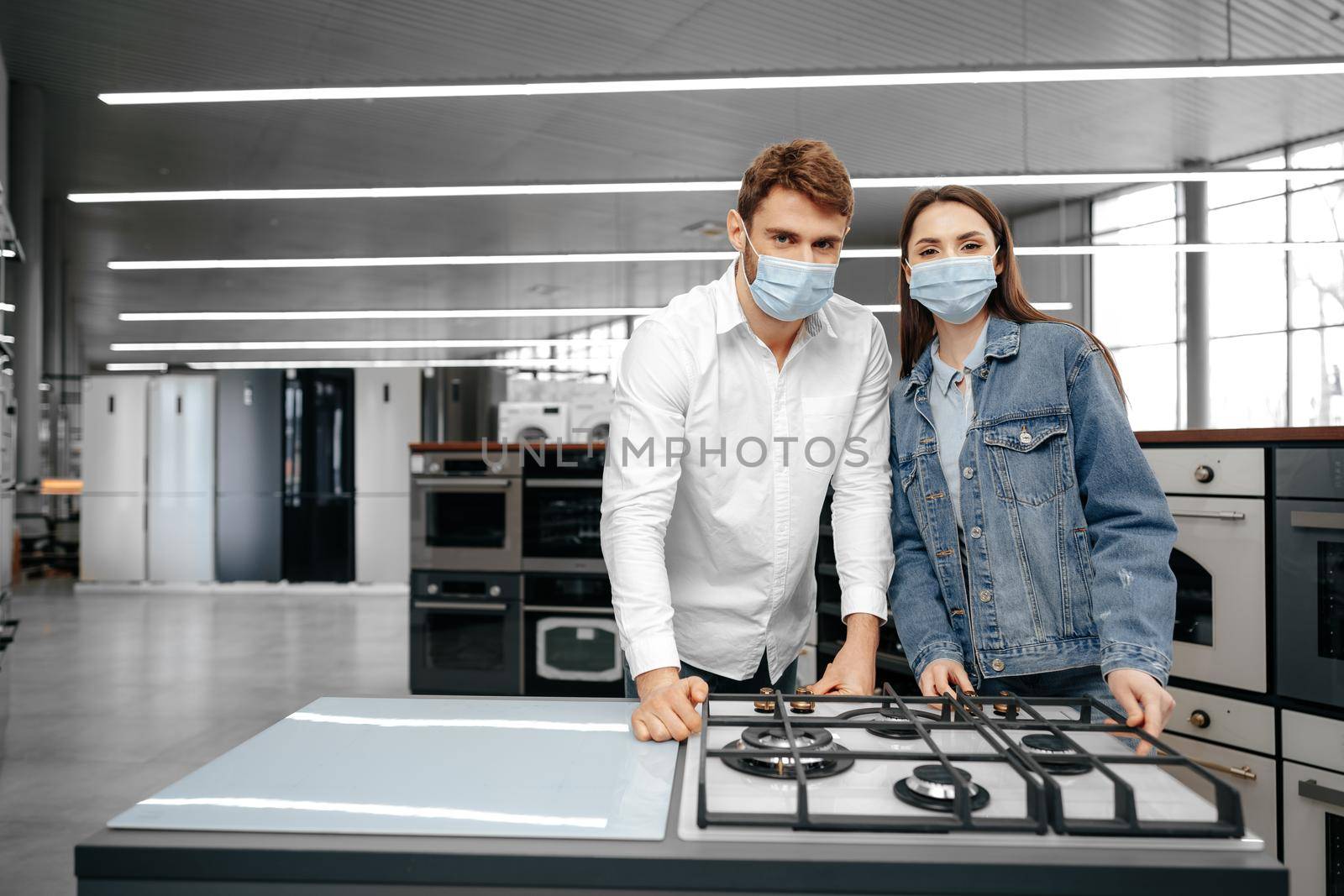 Young couple in medical masks looking at kitchen appliances in a mall, close up