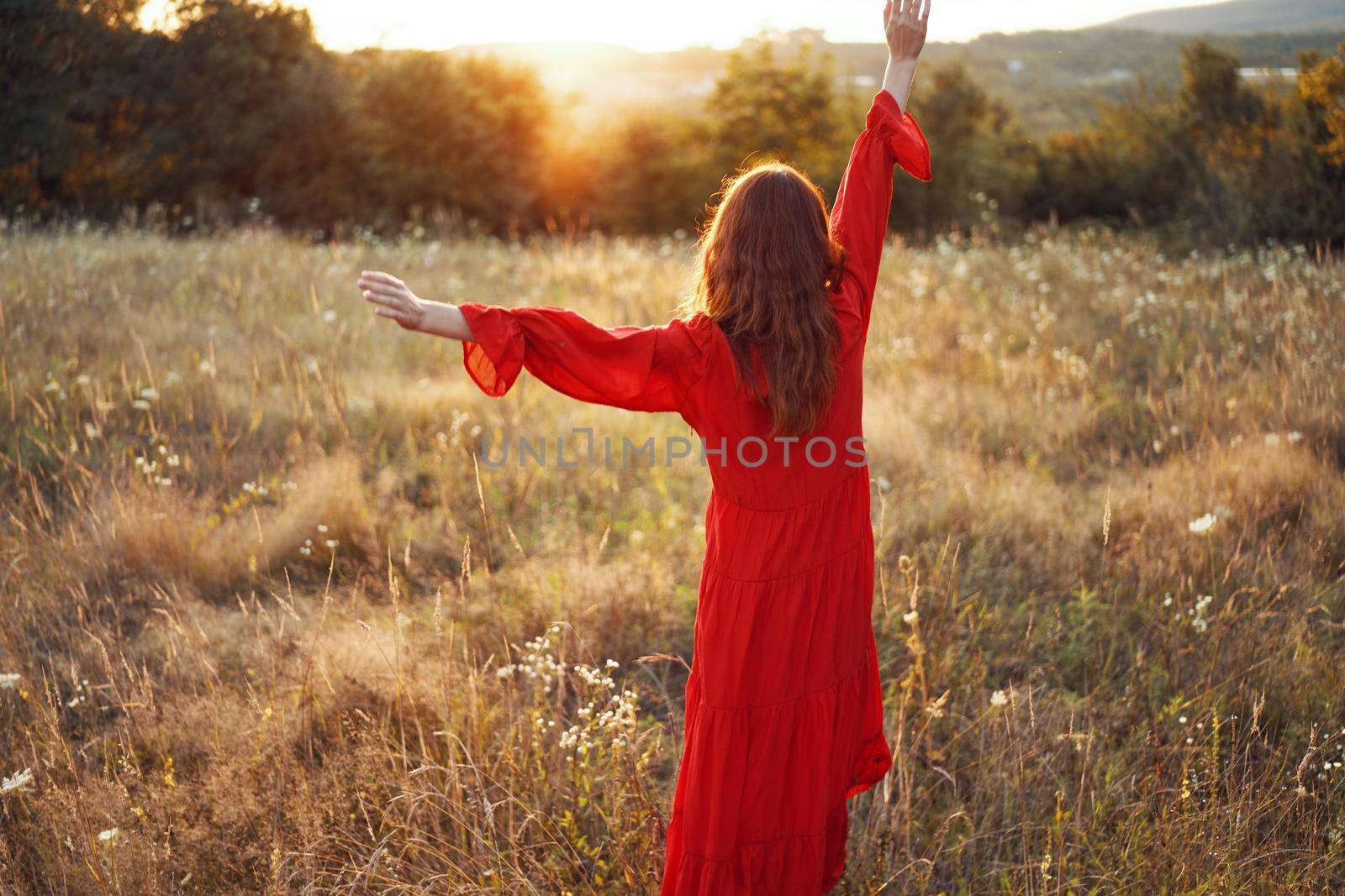 woman in red dress in the field with hands raised up posing. High quality photo