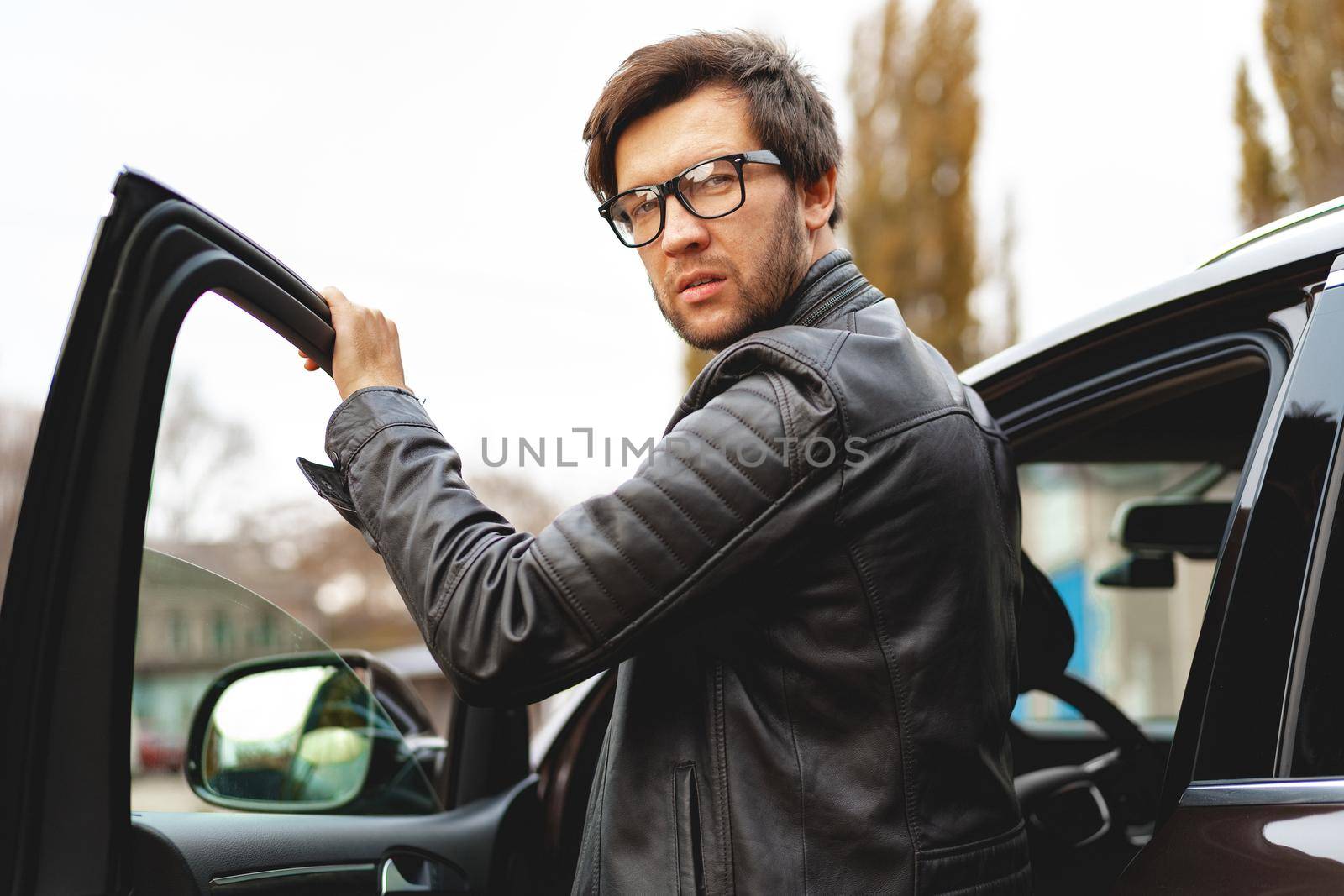 Stylish man in glasses sits in a car, close up portrait