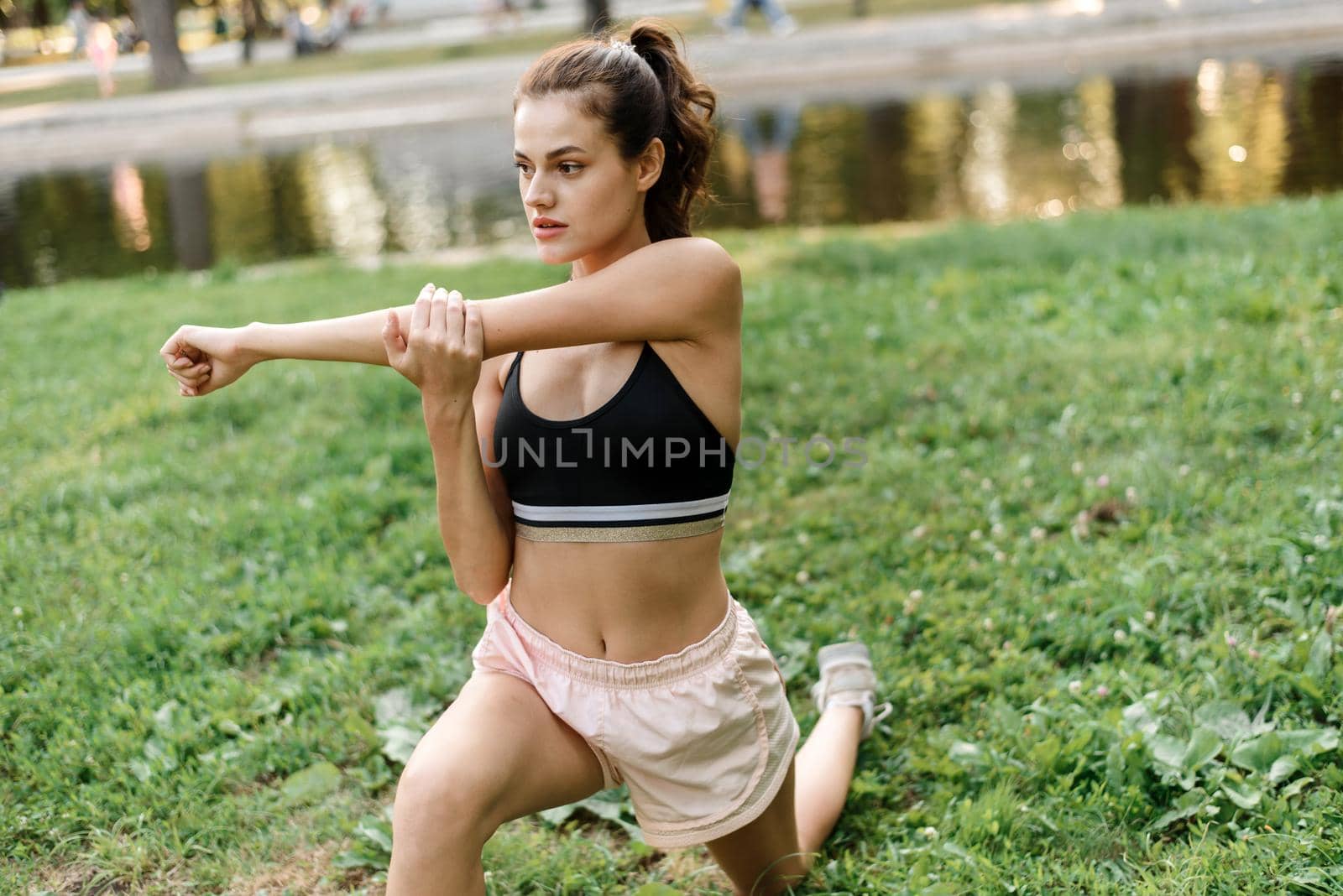 Young woman stretches her arms while doing sports in the park.