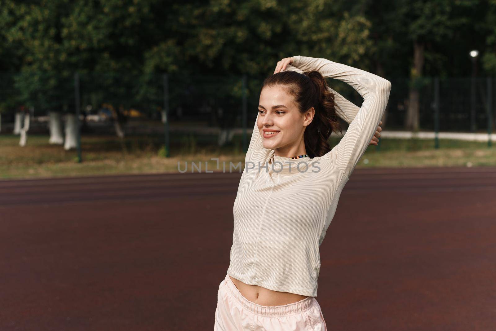 Young woman stretches her arms while playing sports in the stadium.