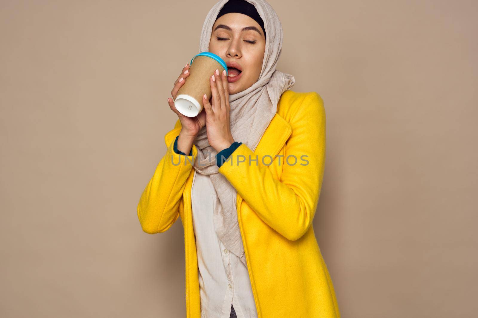 woman in sunglasses in hijab a cup of coffee beige background. High quality photo