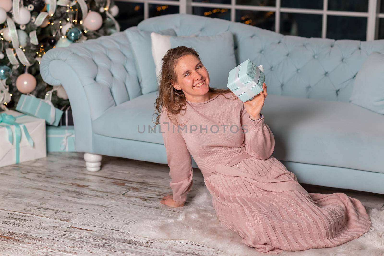 Beautiful middle-aged woman excited opening Christmas presents near the Christmas tree on Christmas eve