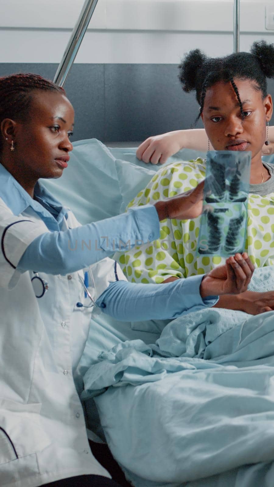 Physician showing radiography results to ill woman in bed. Medical specialist explaining diagnosis on x ray scan to young adult with disease. Doctor talking to patient in hospital ward