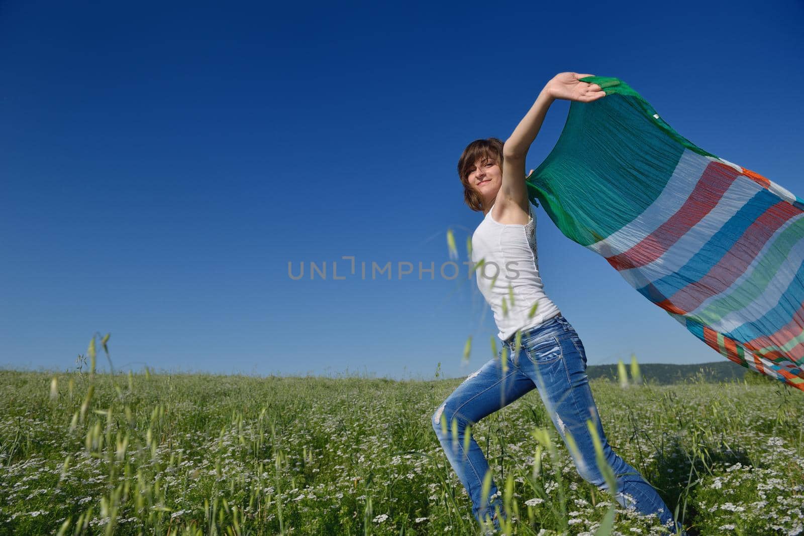 Young woman standing jumping and running  on a wheat field with blue sky in  background at summer day representing healthy life and agriculture concept