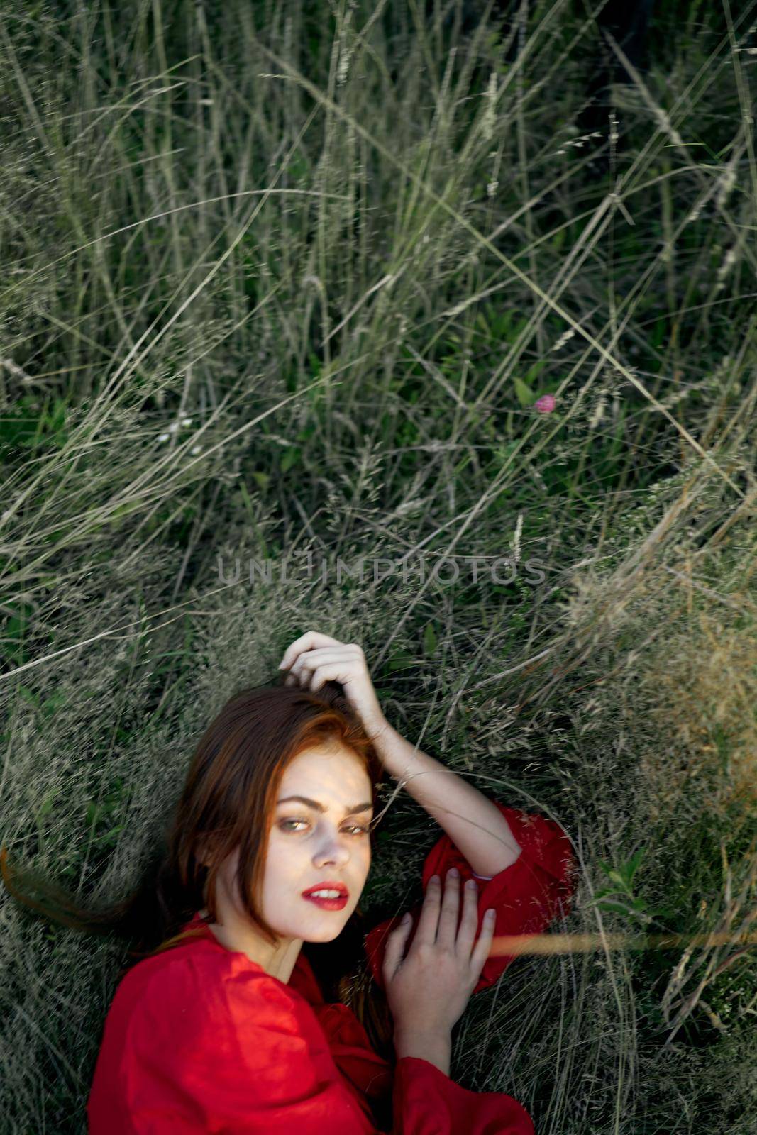 pretty woman in red dress lies on the grass posing top view. High quality photo