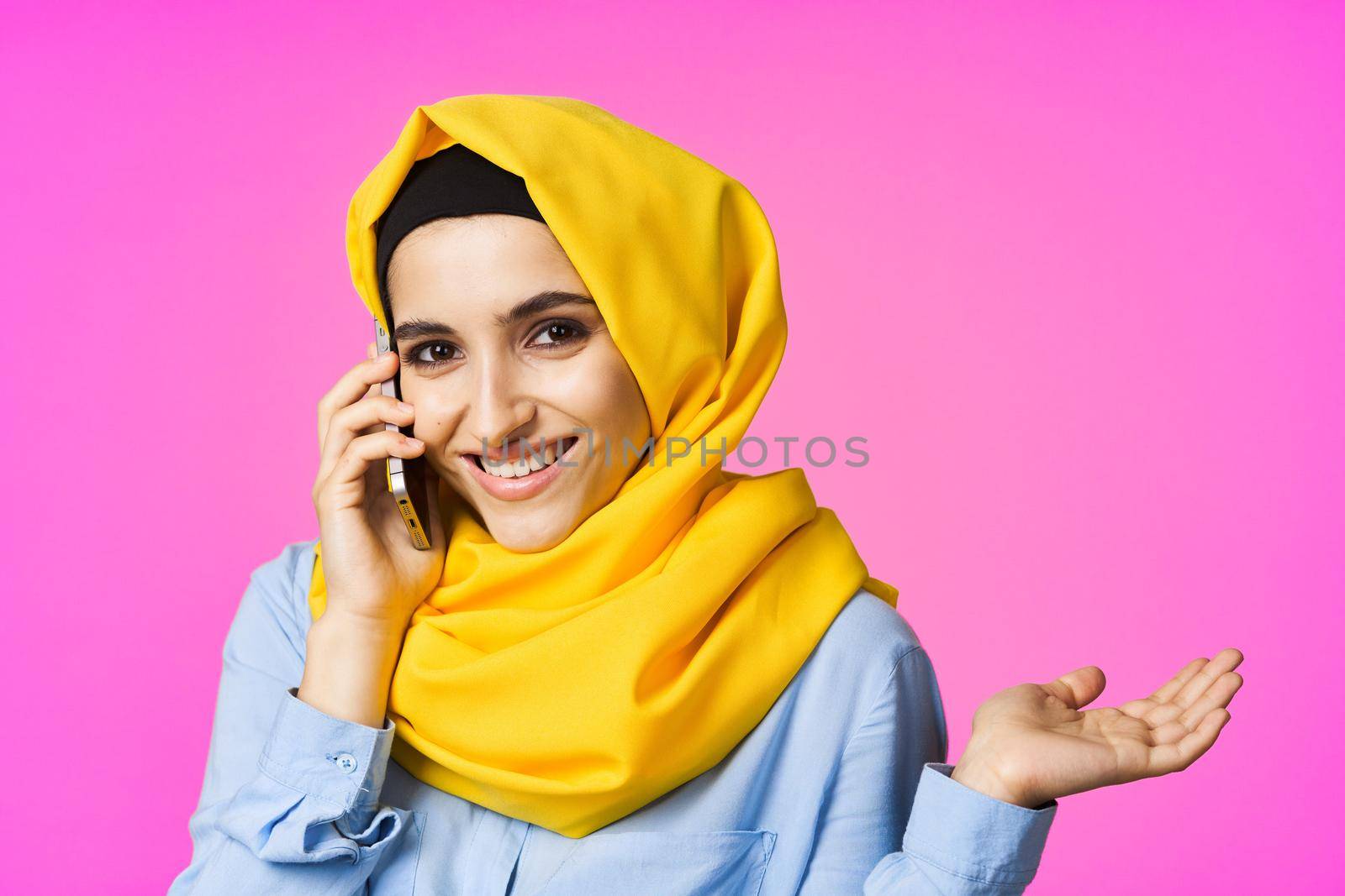 muslim woman in yellow hijab talking on the phone pink technology background. High quality photo