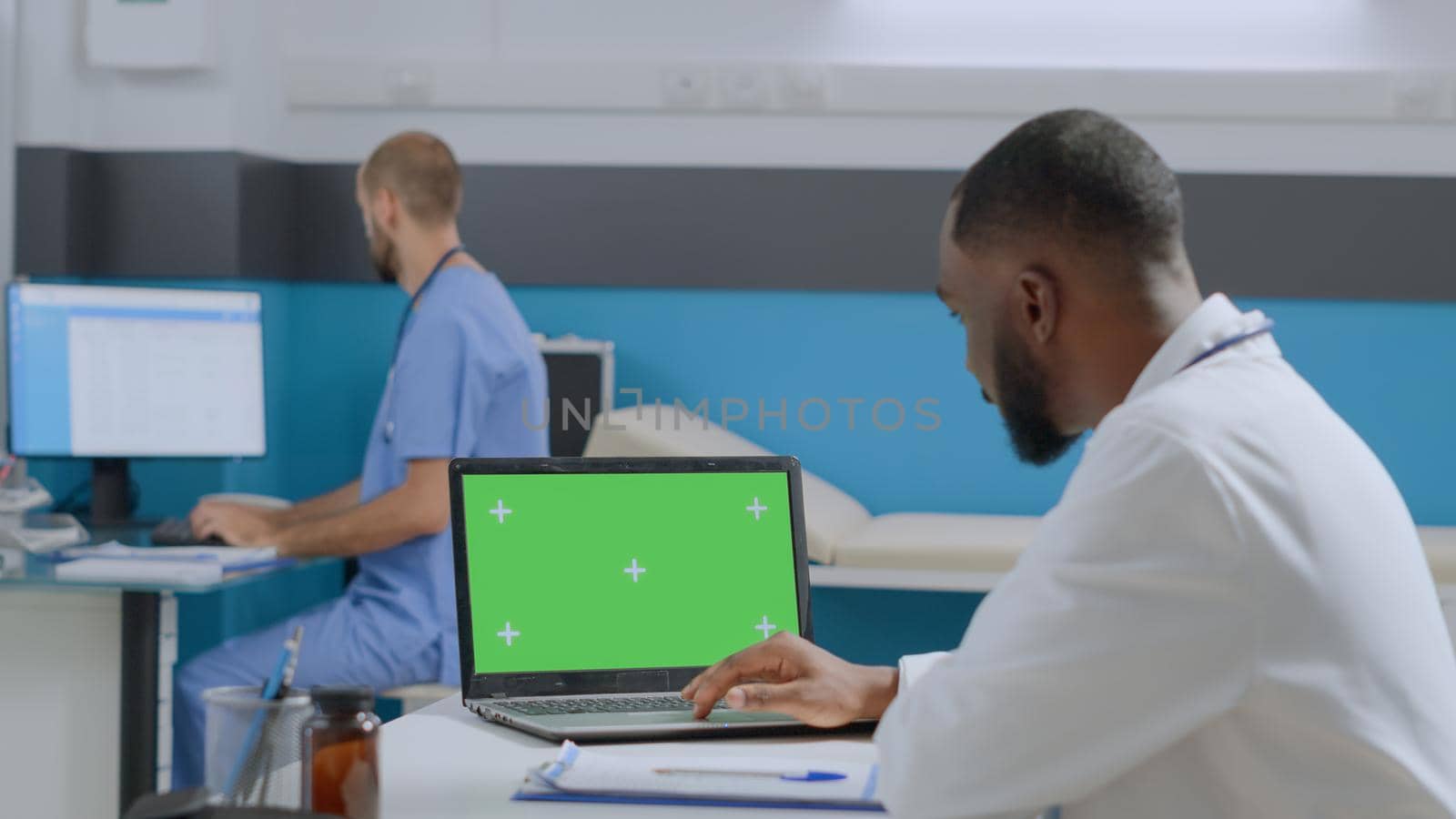 African american physician doctor looking at mock up green screen chroma key laptop computer by DCStudio